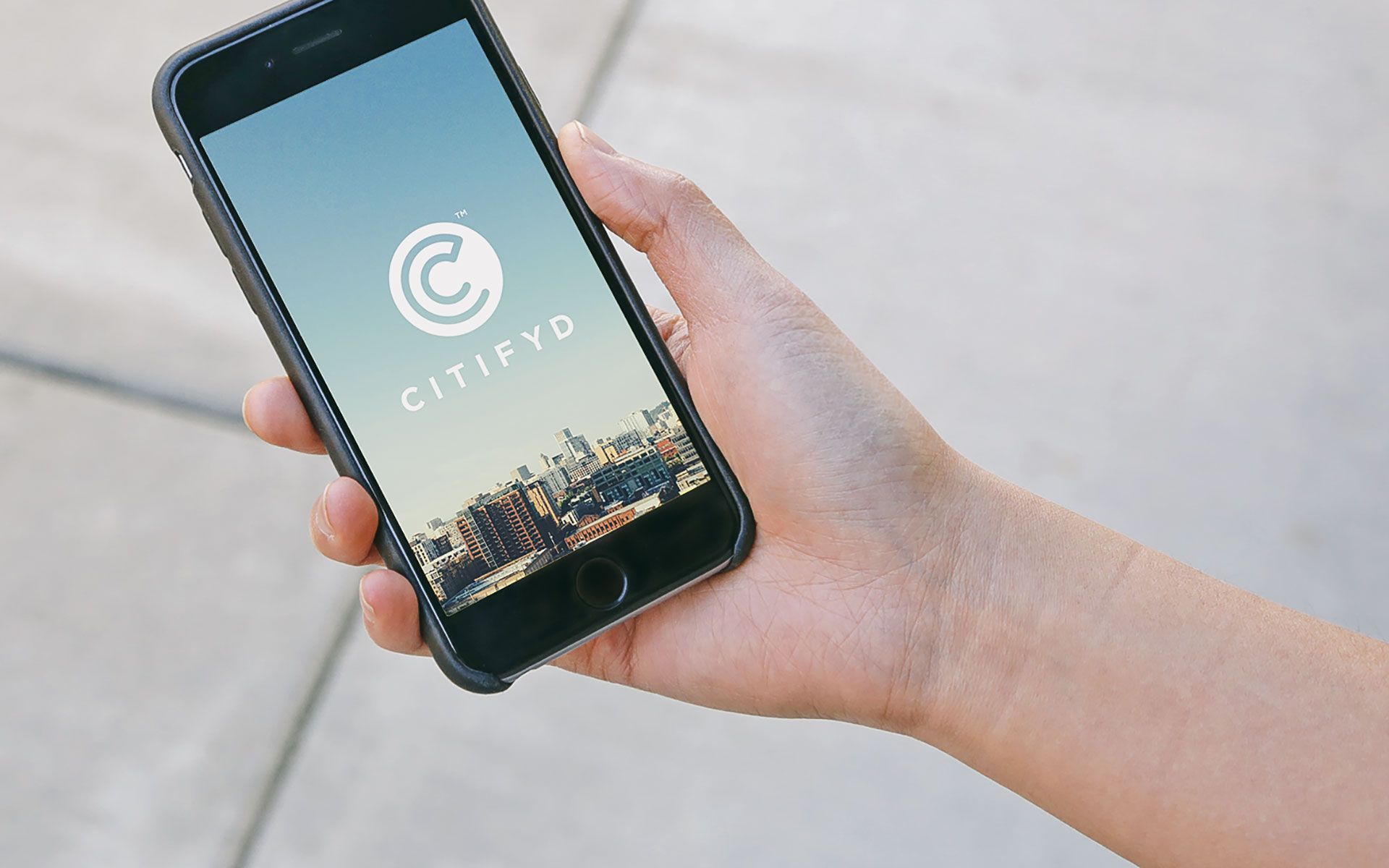 Hand holding a mobile phone with an image of a city skyline and the Citifyd logo