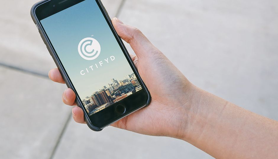 Hand holding a mobile phone with an image of a city skyline and the Citifyd logo