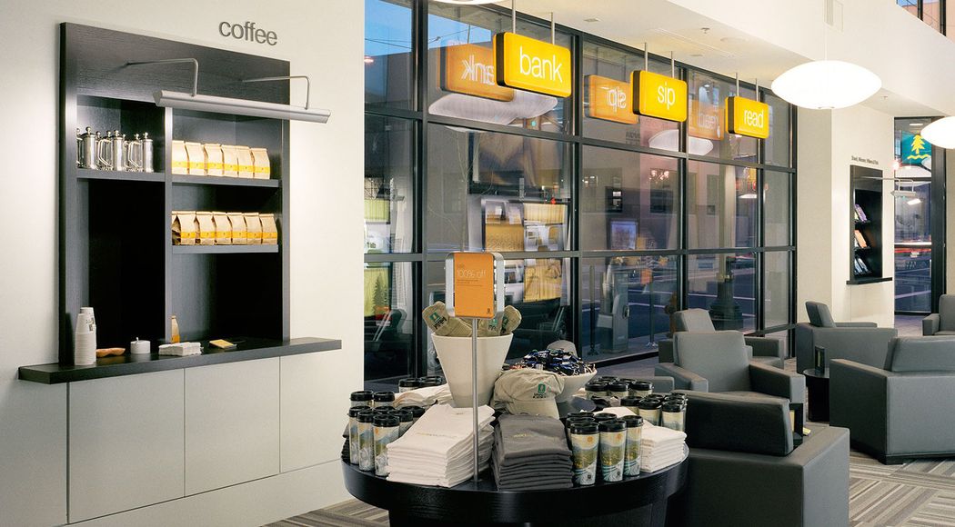 Umpqua Bank lobby, featuring a coffee station, a group of lounge chairs, and a table with travel mugs, hats, shirts, and slippers on it