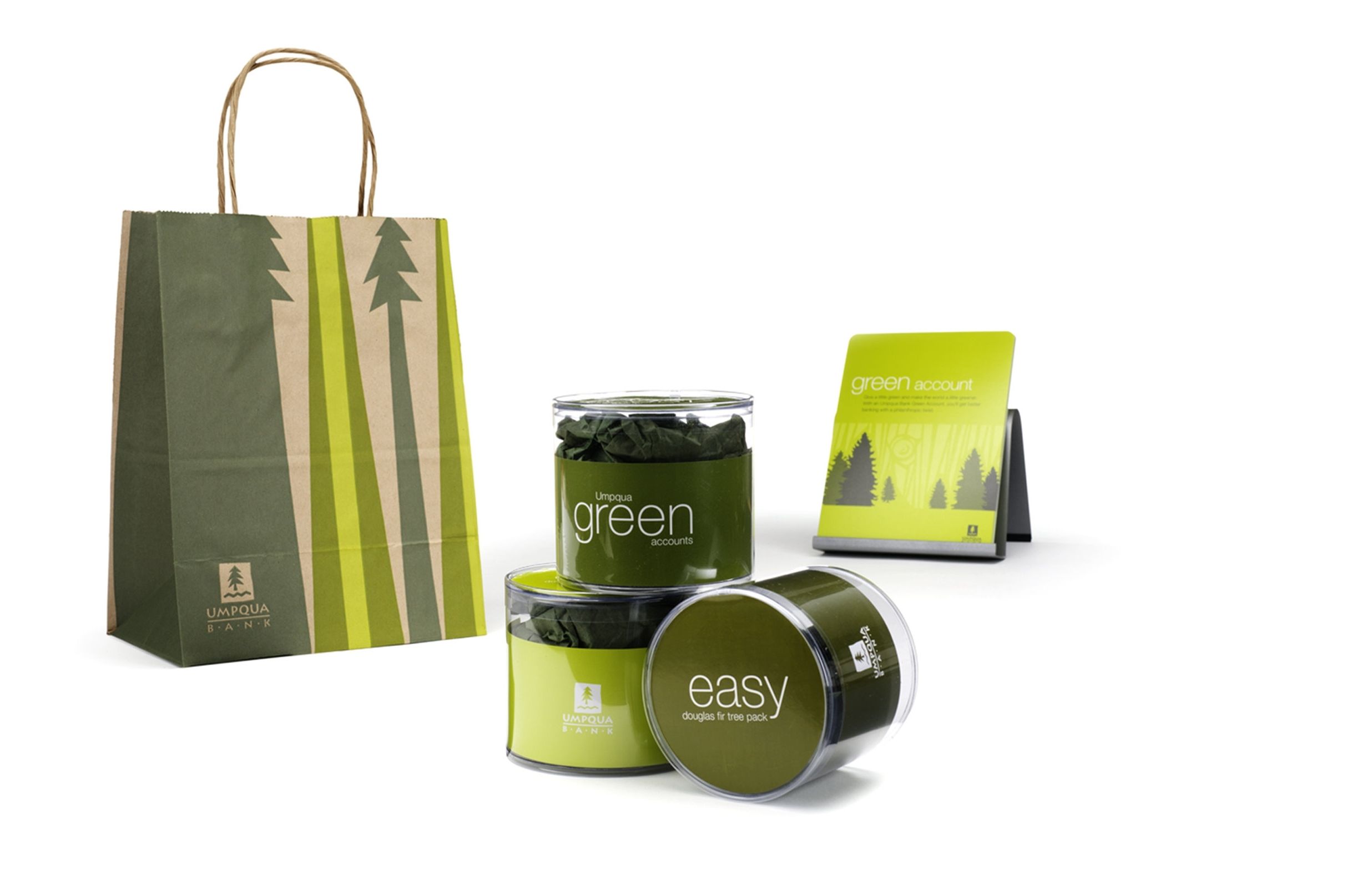 Paper bag with the Umpqua Bank logo and green illustrated trees, three jars containing Douglas fir cones, and a green business card that says “green account”
