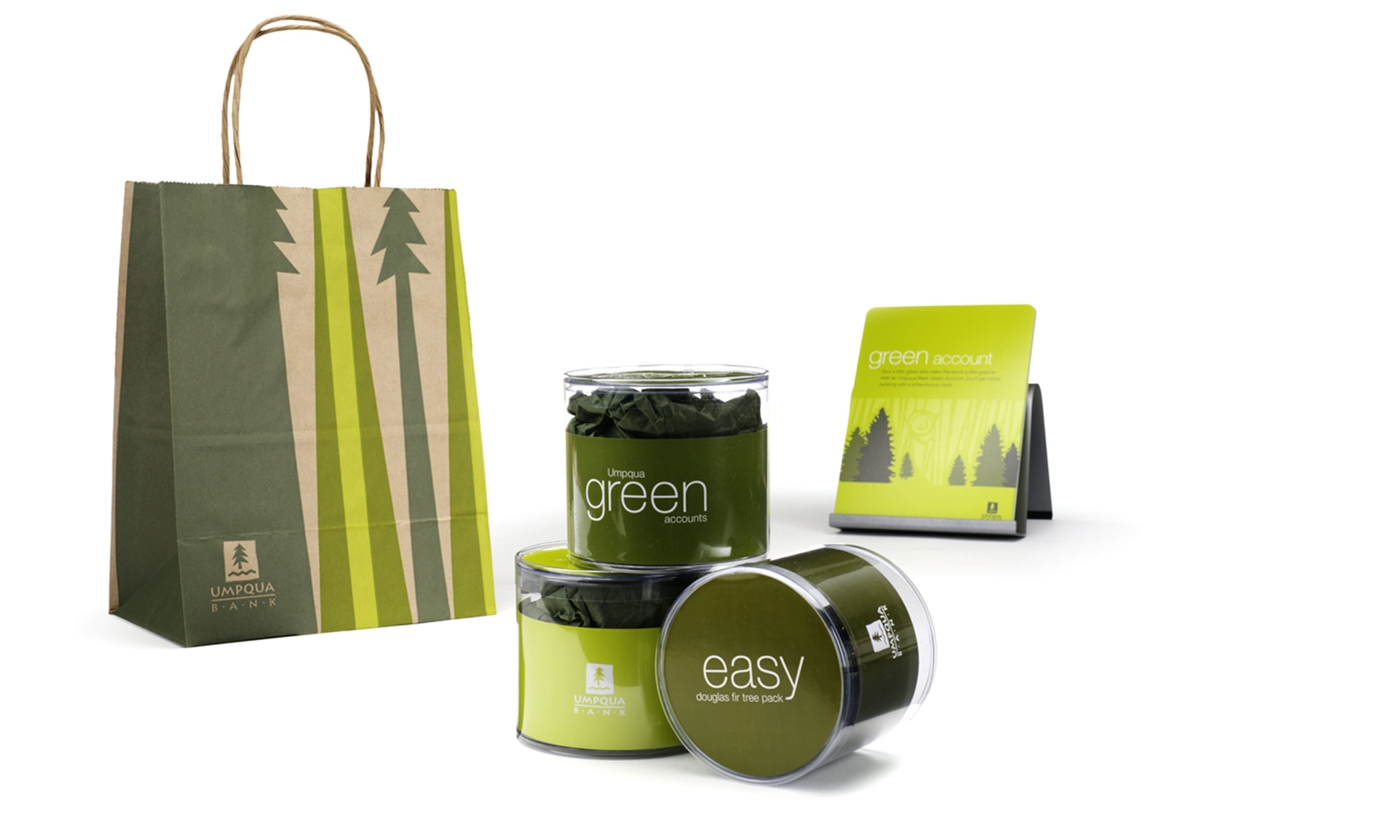 Paper bag with the Umpqua Bank logo and green illustrated trees, three jars containing Douglas fir cones, and a green business card that says “green account”