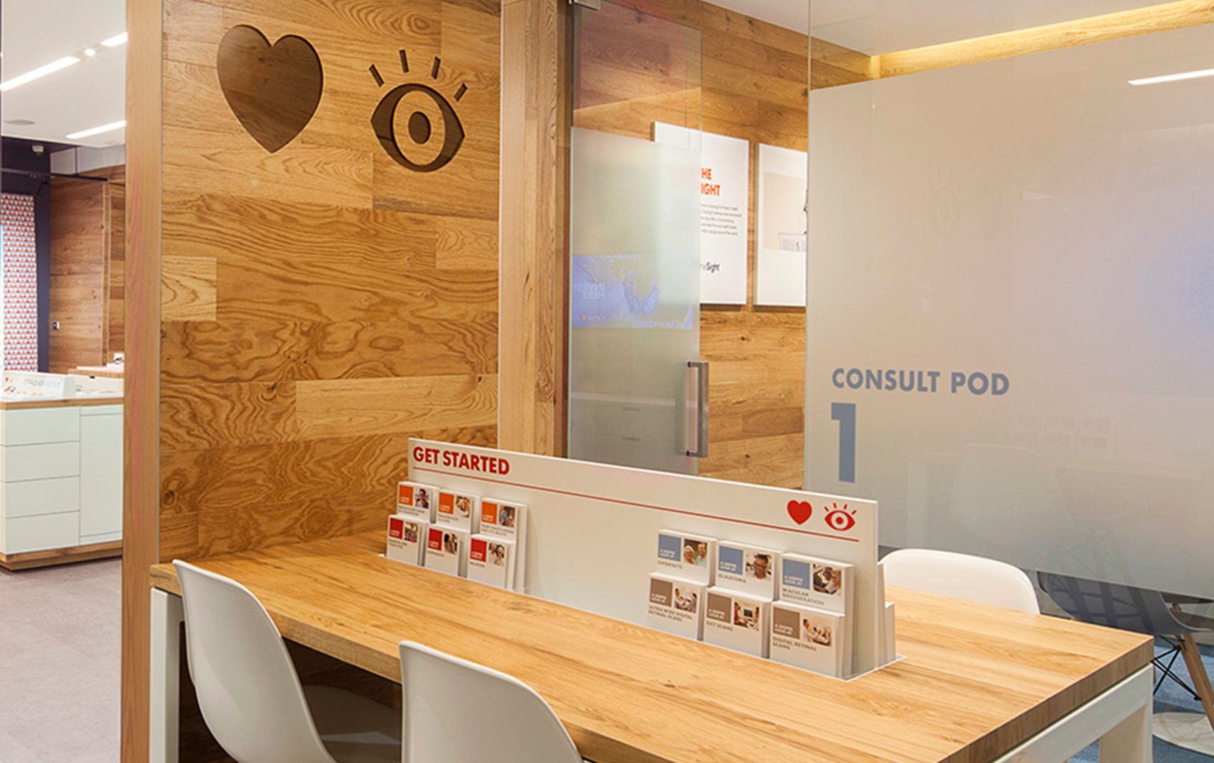 Wooden wall with a heart and an illustrated eye carved into it, next to a wooden desk with four white chairs and a table divider that reads “Get Started”