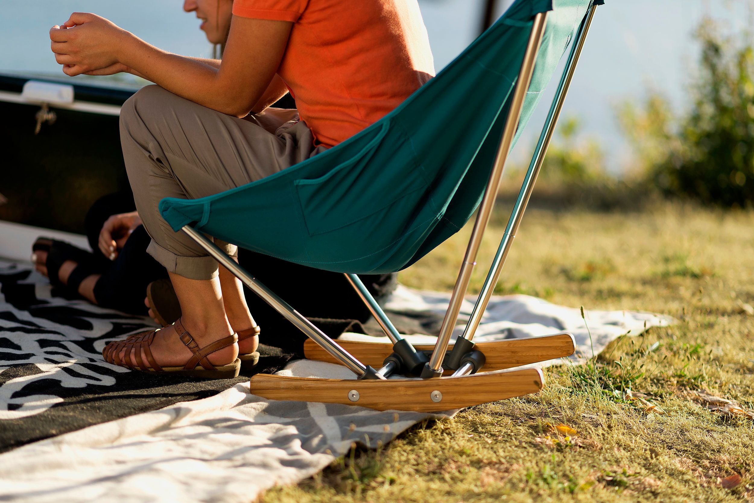 Person sitting on a camping chair that has four metal supports attached to two curved pieces of wood on the bottom
