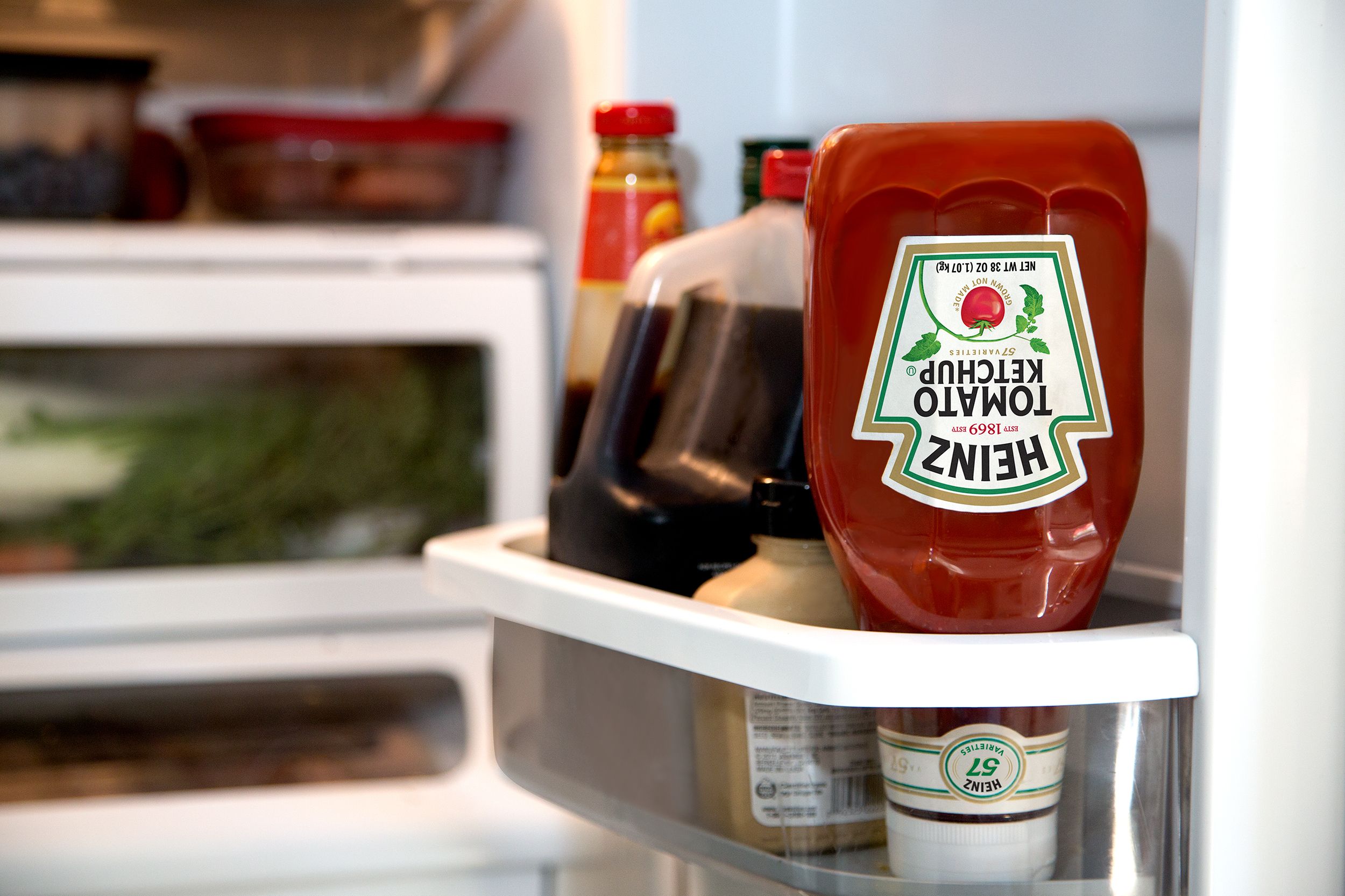 Heinz ketchup bottle placed upside down in a refrigerator next to other condiments