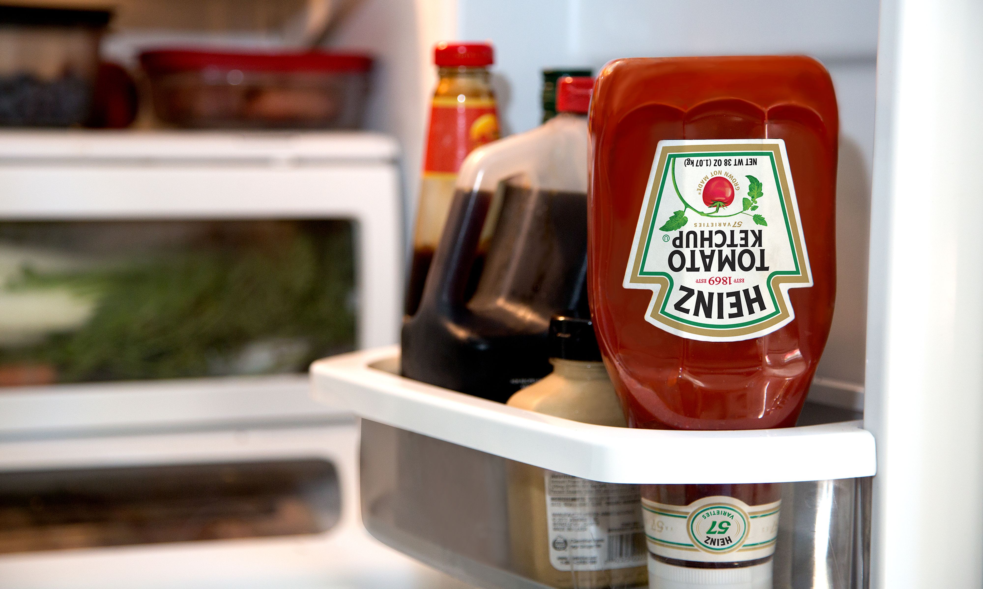 Heinz ketchup bottle placed upside down in a refrigerator next to other condiments