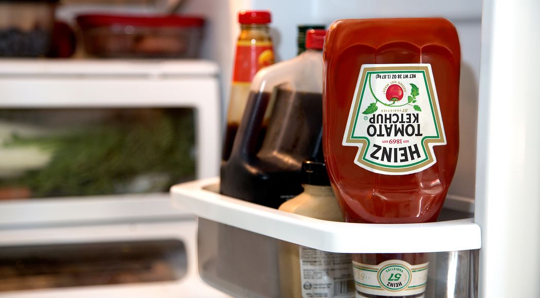 Heinz ketchup bottle placed upside down in a refrigerator next to other condiments