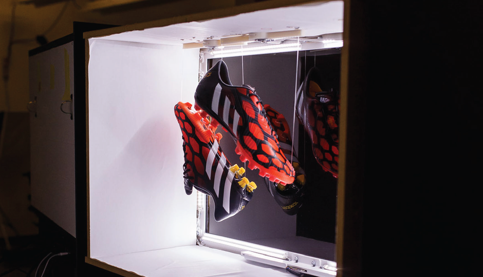 Two red cleats suspended on string inside of a white illuminated box