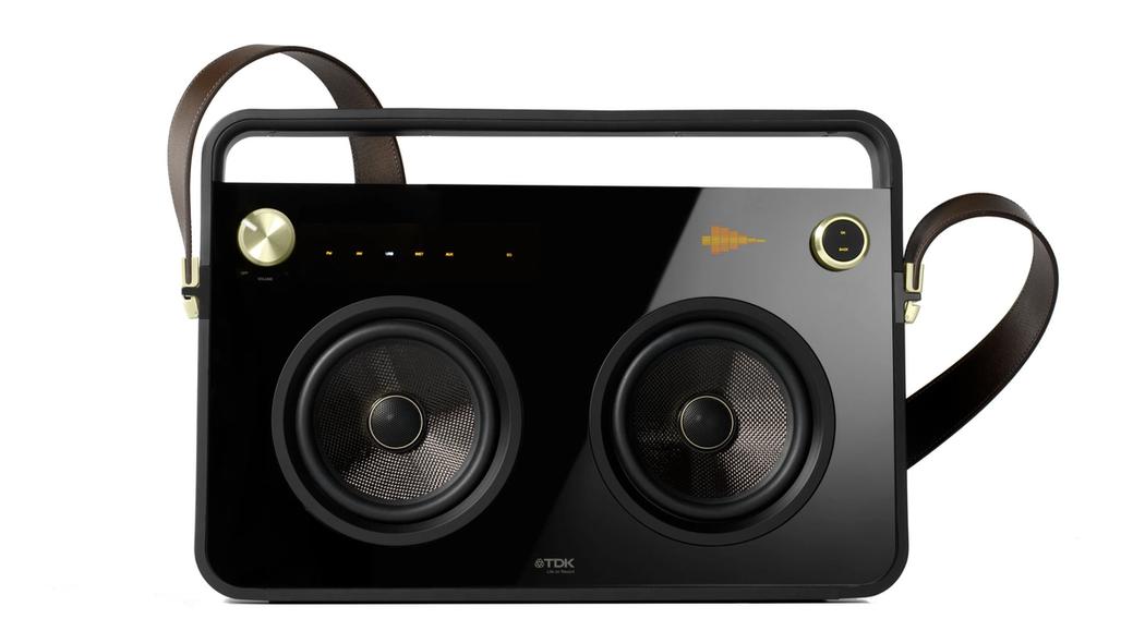 Black boombox with a gold knob in the top left, two speakers in the middle, and a brown leather strap buckled to the sides