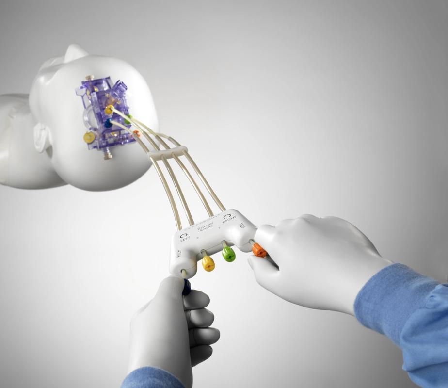 Person wearing white gloves controlling a surgical device that is attached to a mannequin’s head by four rubber tubes