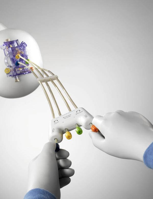 Person wearing white gloves controlling a surgical device that is attached to a mannequin’s head by four rubber tubes