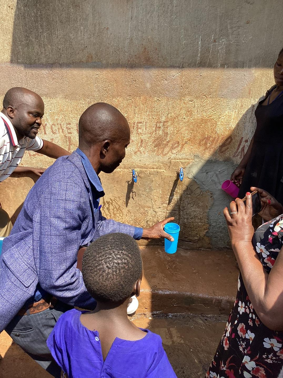 A community member helping his family drink from a completed Give Water Give Life water system.