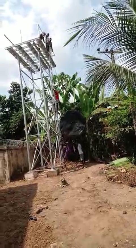 Workers lifting a water tank beside a tall metal support structure.