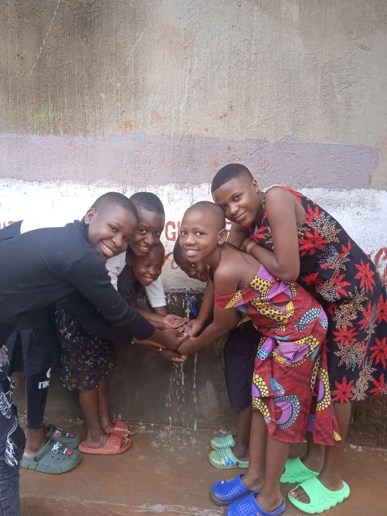 Children gathered around a running tap at a completed water point, washing their hands.