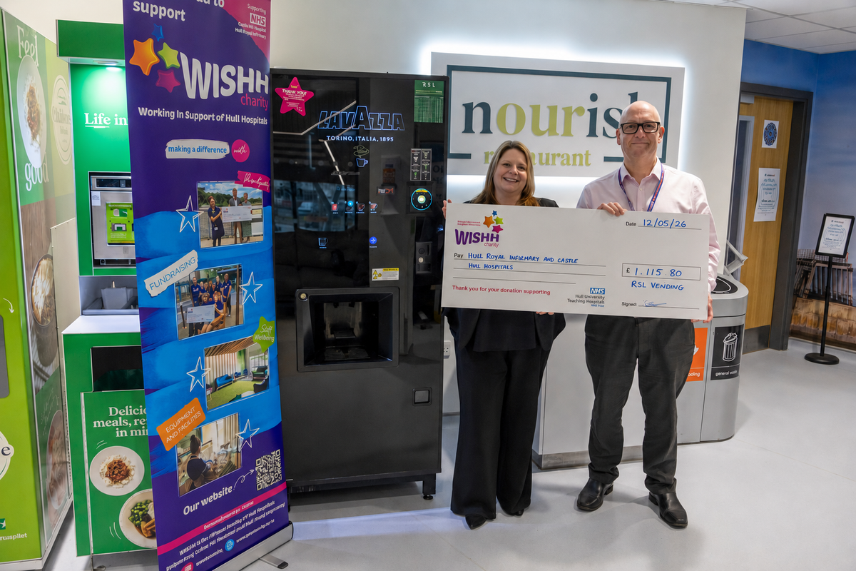 Two staff members holding a large cheque in front of vending machine