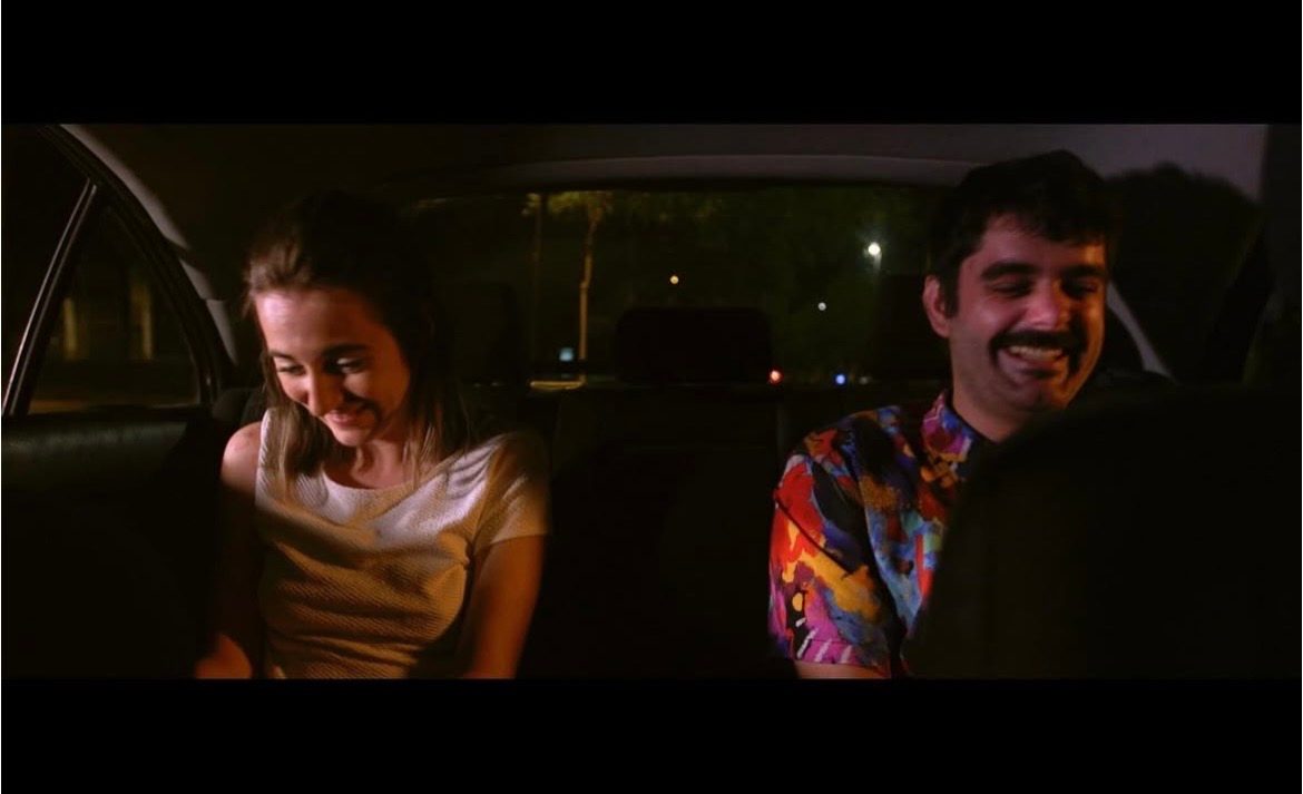 Fotograma del corto: Cecilia Mansilla y su acompañante riéndose en el asiento trasero de un coche, de noche