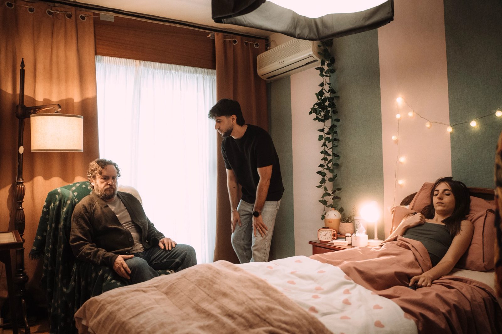 Escena de rodaje en un dormitorio: una mujer tumbada en la cama y dos hombres junto a ella