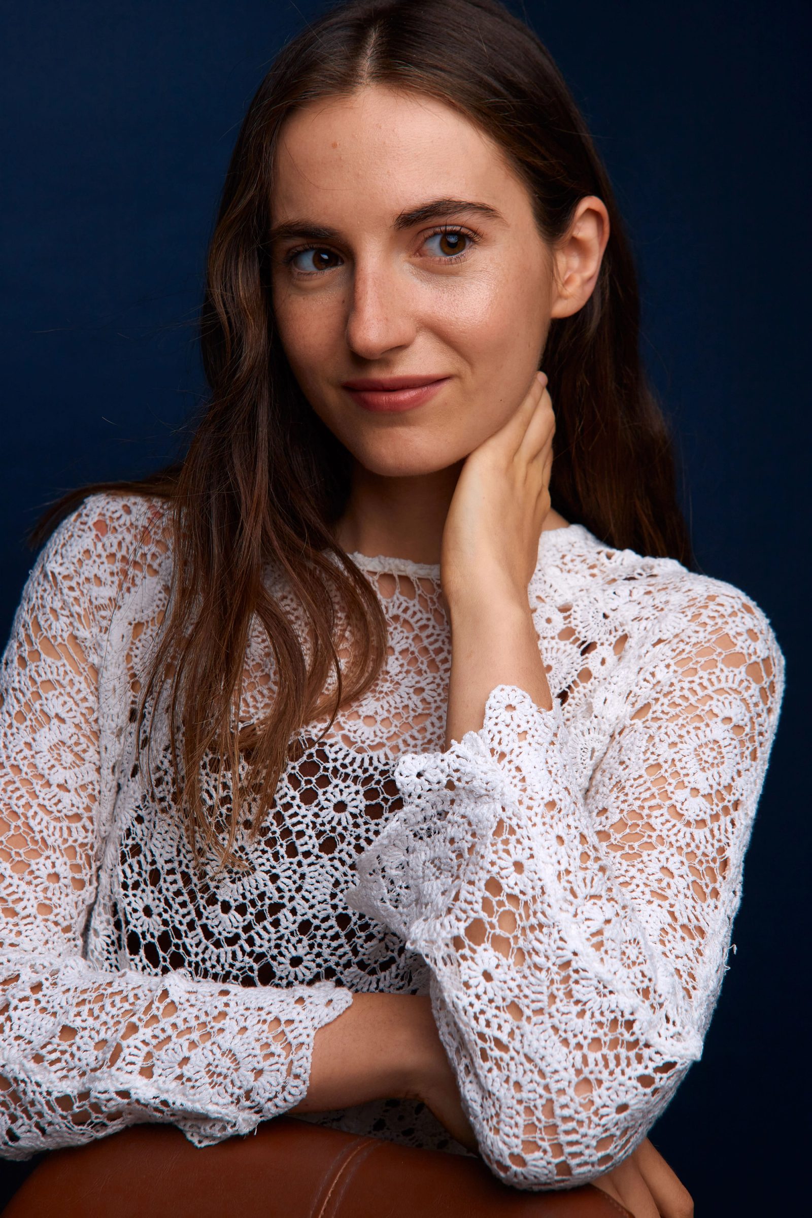 Retrato de Cecilia Mansilla con blusa blanca de encaje, apoyando la mano en el cuello, sobre fondo azul