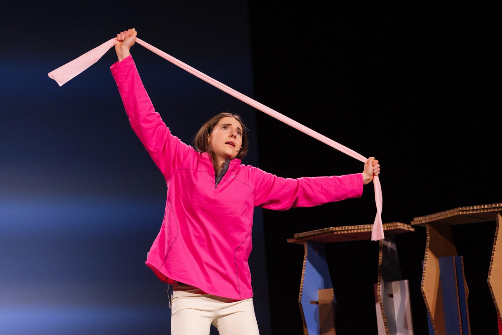 Cecilia Mansilla en escena con chaqueta rosa, tensando una cinta de papel entre las manos