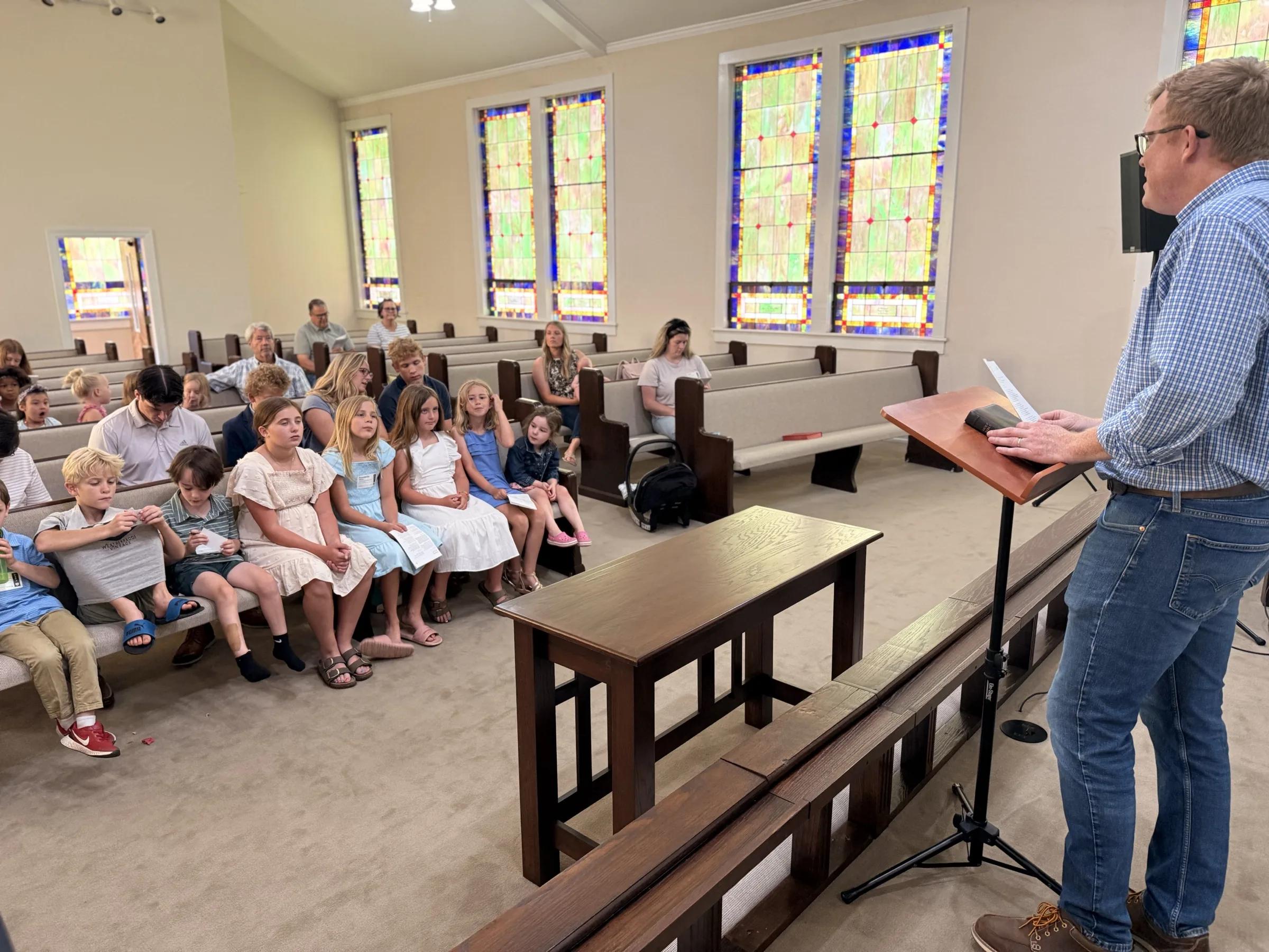Children and adults gathered together beneath stained-glass windows.