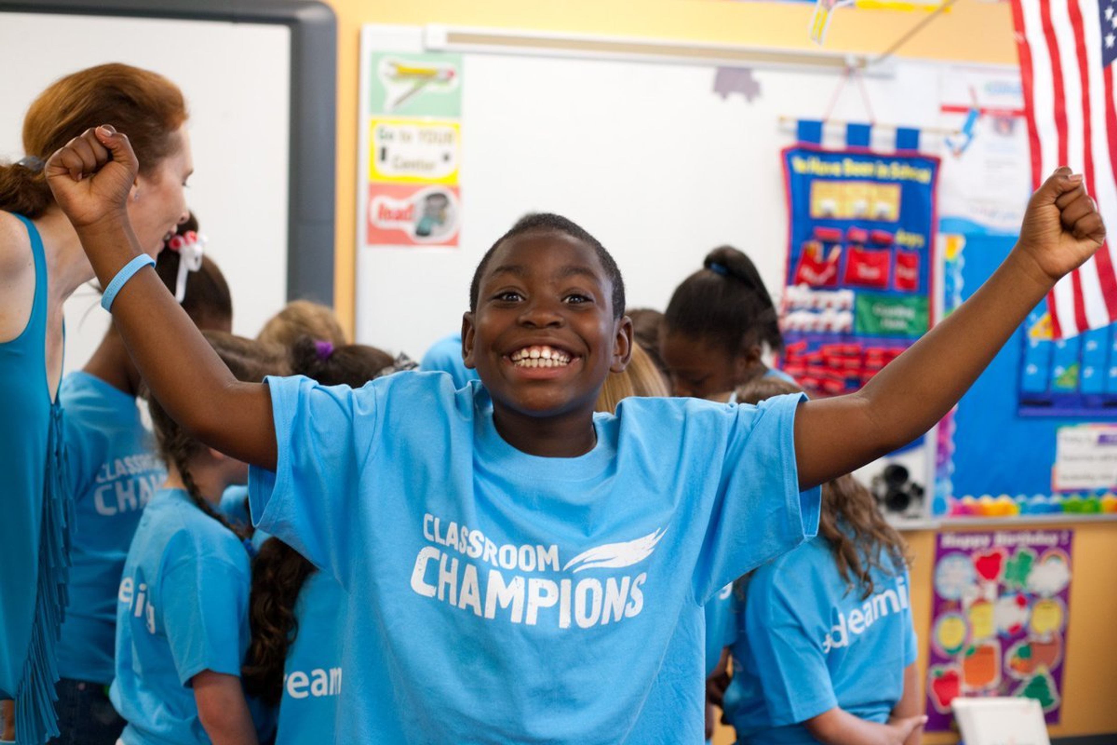 A student raises his arms in celebration wearing a Classroom Champions t-shirt in his classroom.
