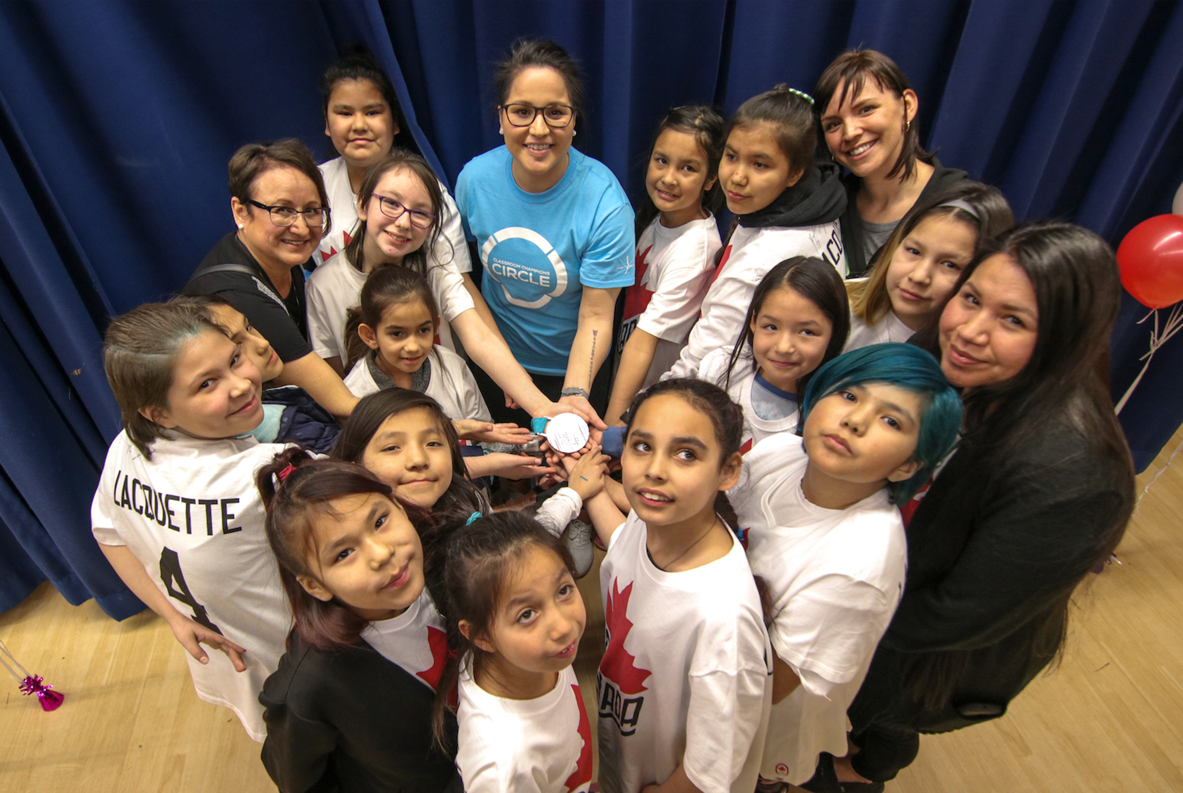 A mentor and students in Team Canada shirts join hands together in a group huddle.