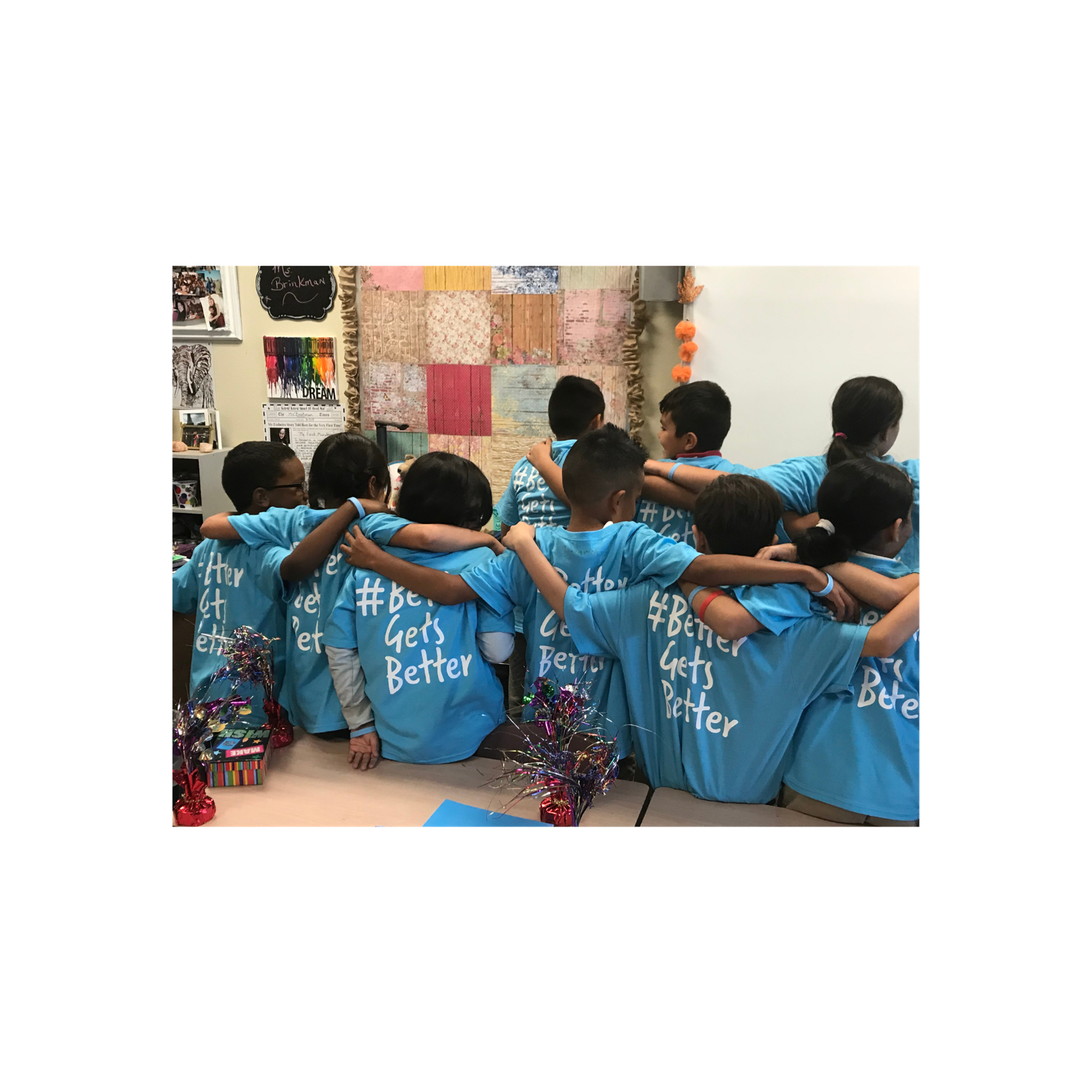 Students stand arm-in-arm in a classroom wearing matching shirts reading "#Better Gets Better."