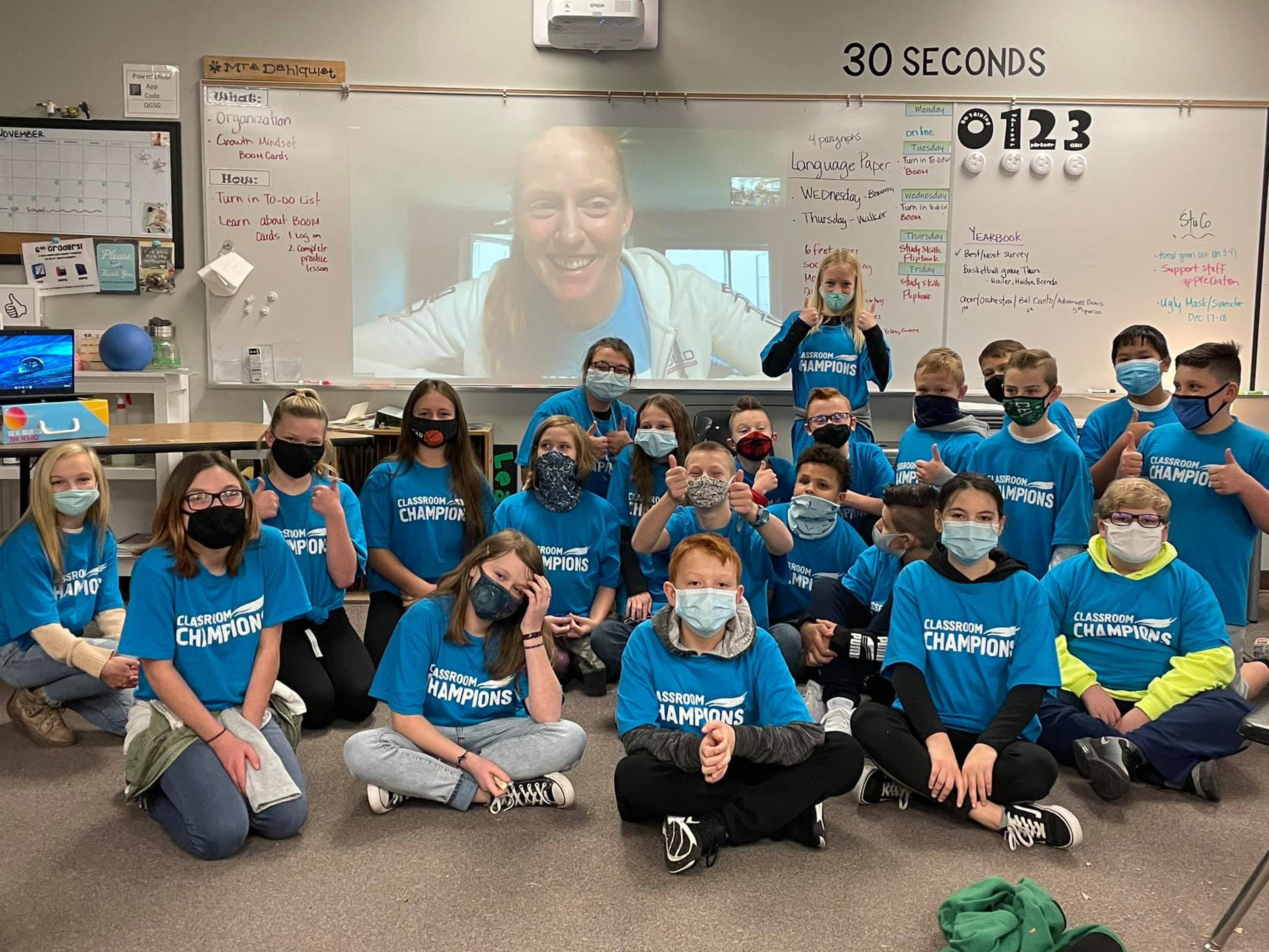 Students in Classroom Champions t-shirts pose for a video call with their athlete mentor projected on screen.