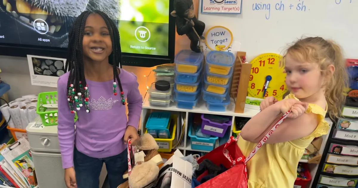 Two students in a classroom hold shopping bags of donated items for a service learning project.