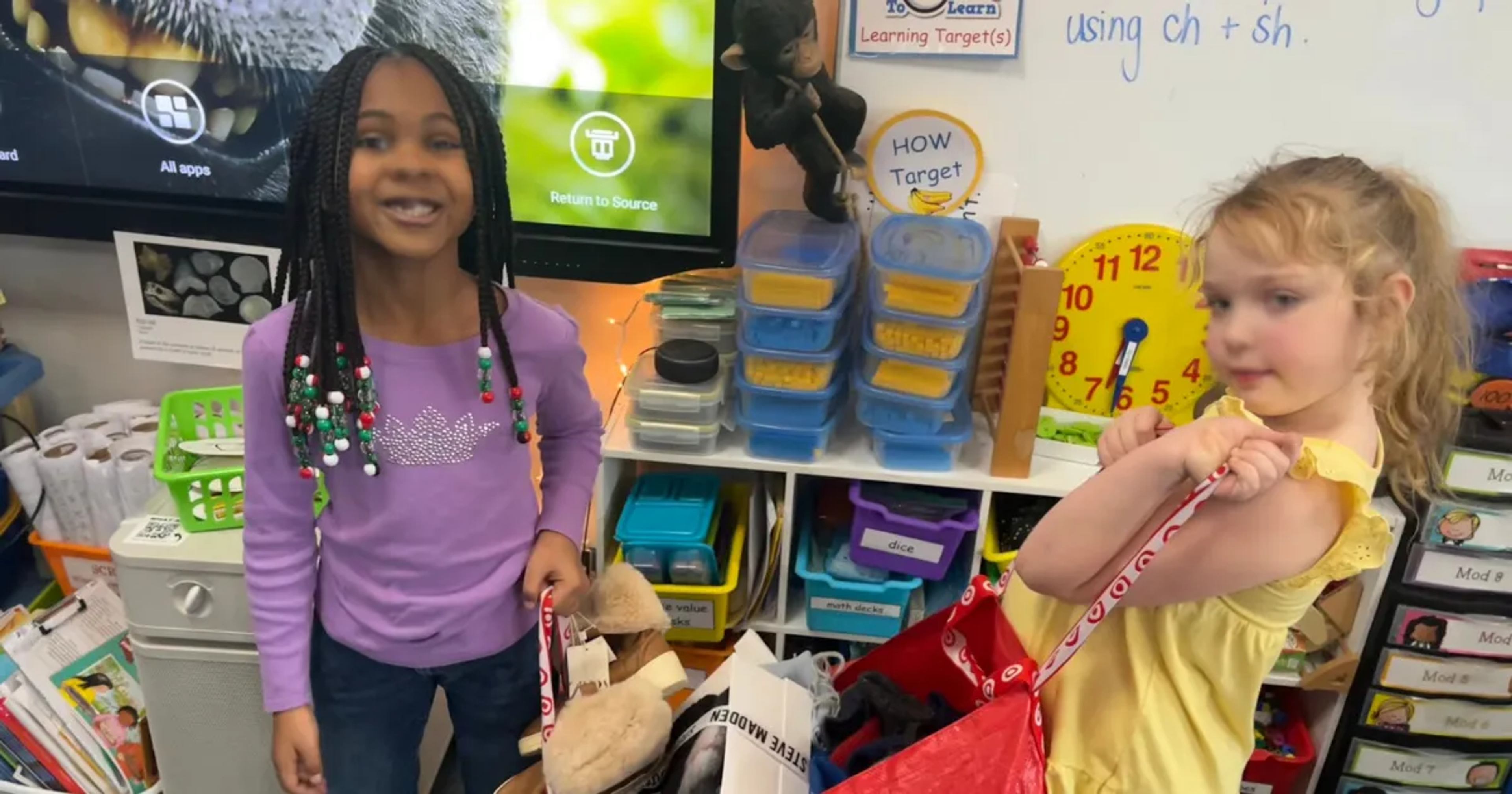 Two students in a classroom hold shopping bags of donated items for a service learning project.