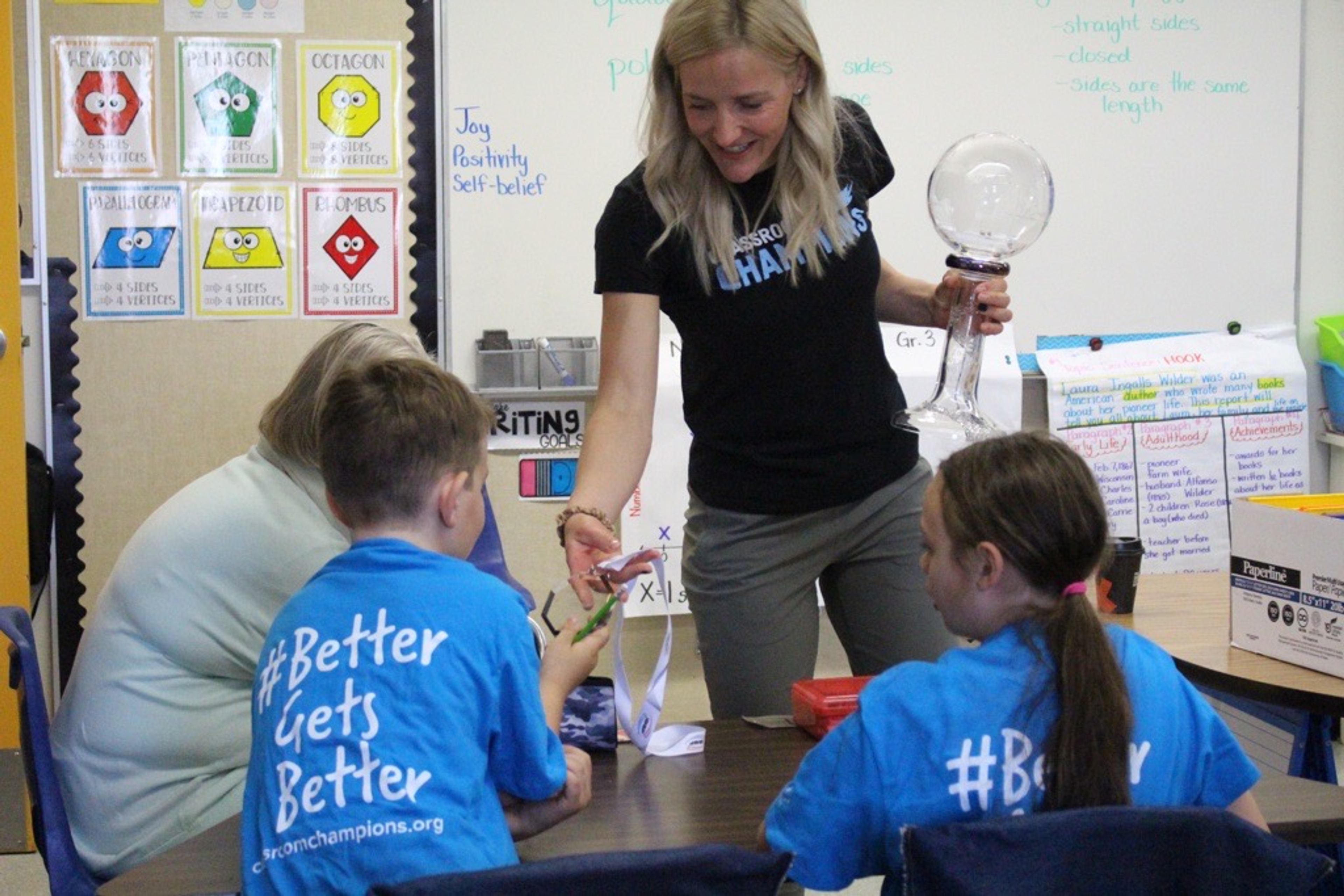 A Classroom Champions mentor holds a snow globe while visiting students wearing #BetterGetsBetter shirts.