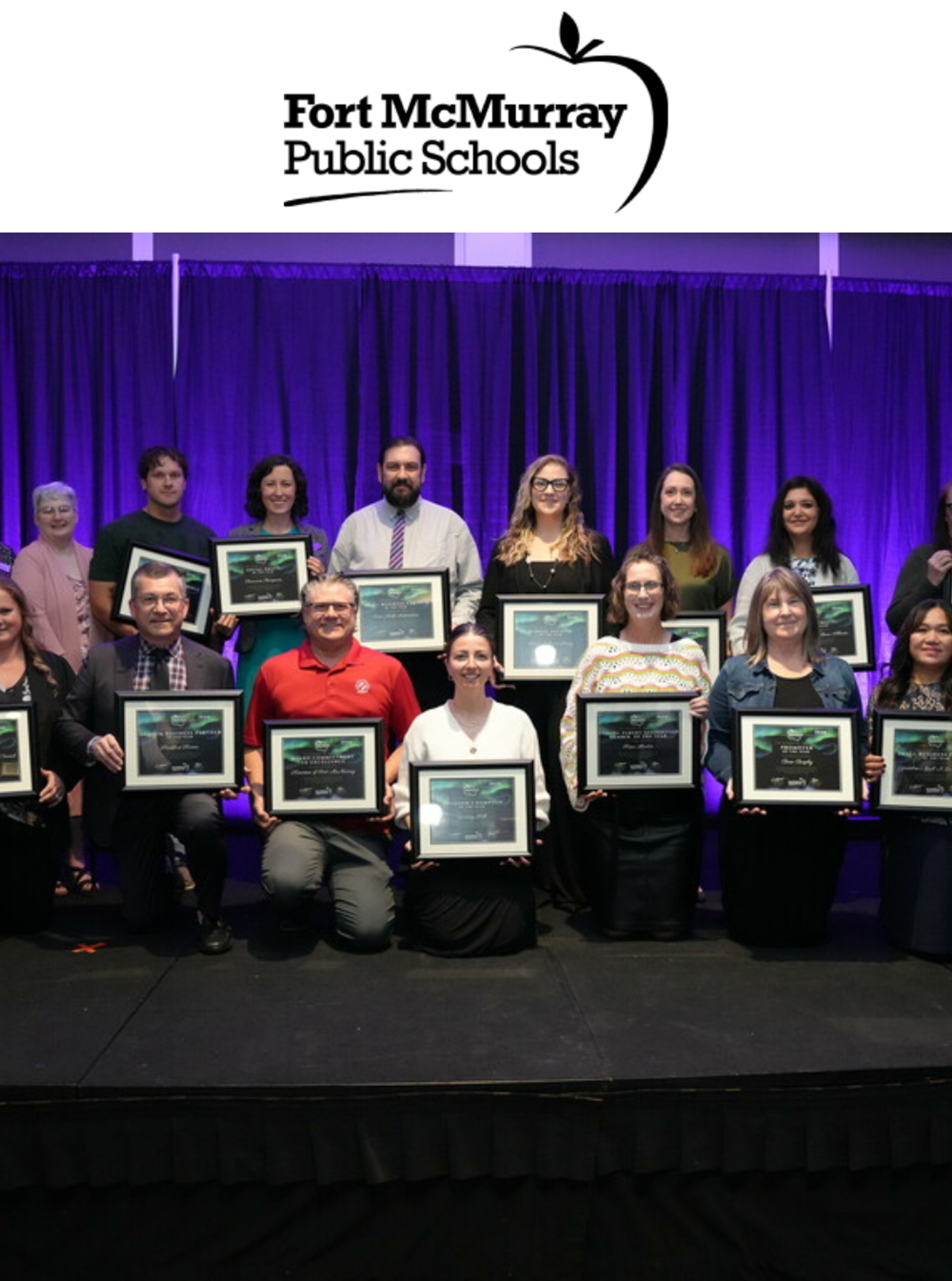Fort McMurray Public Schools logo above a group of award recipients holding framed certificates on stage.
