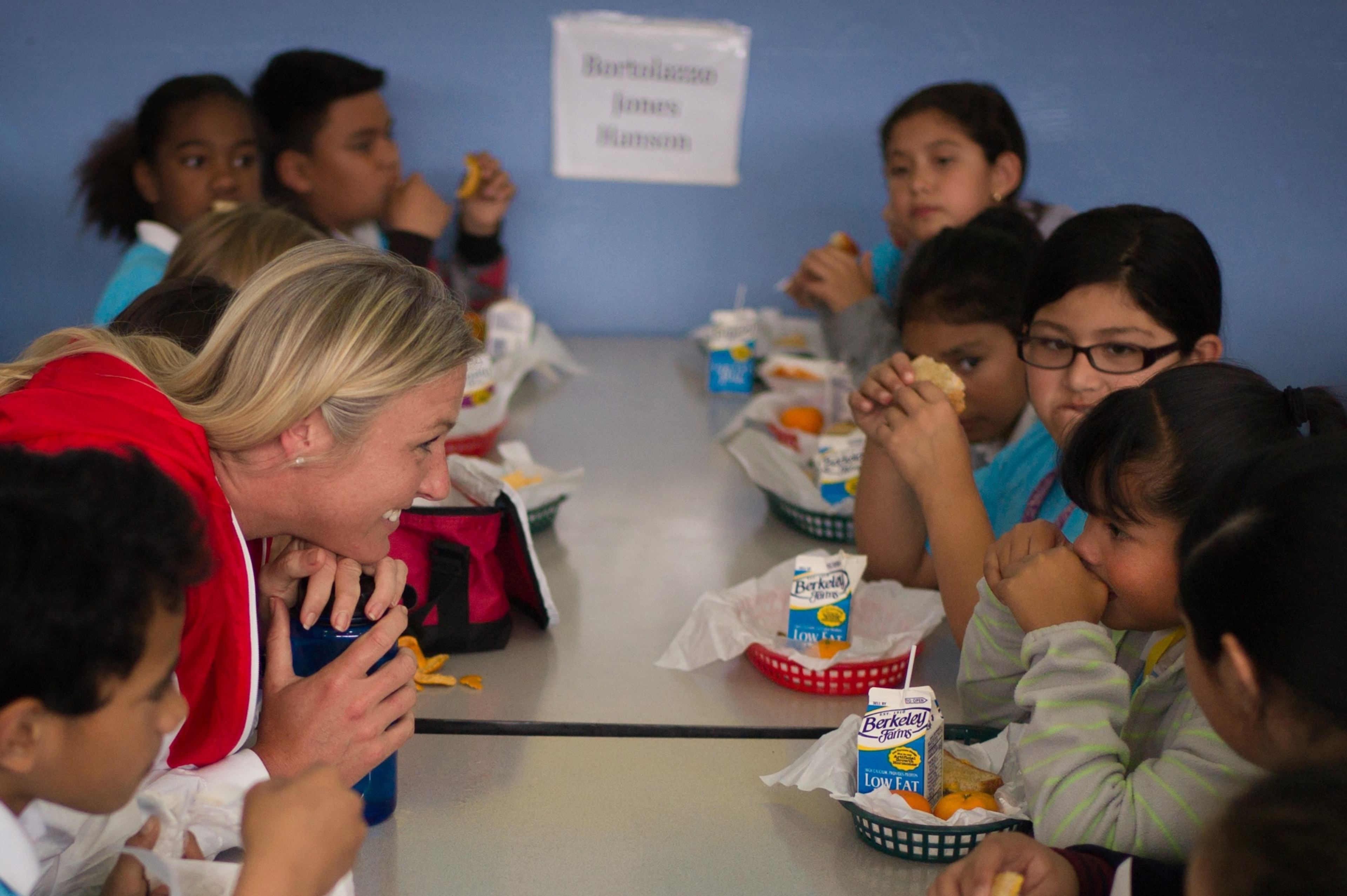 A mentor smiles and chats with students during lunch in a school cafeteria.