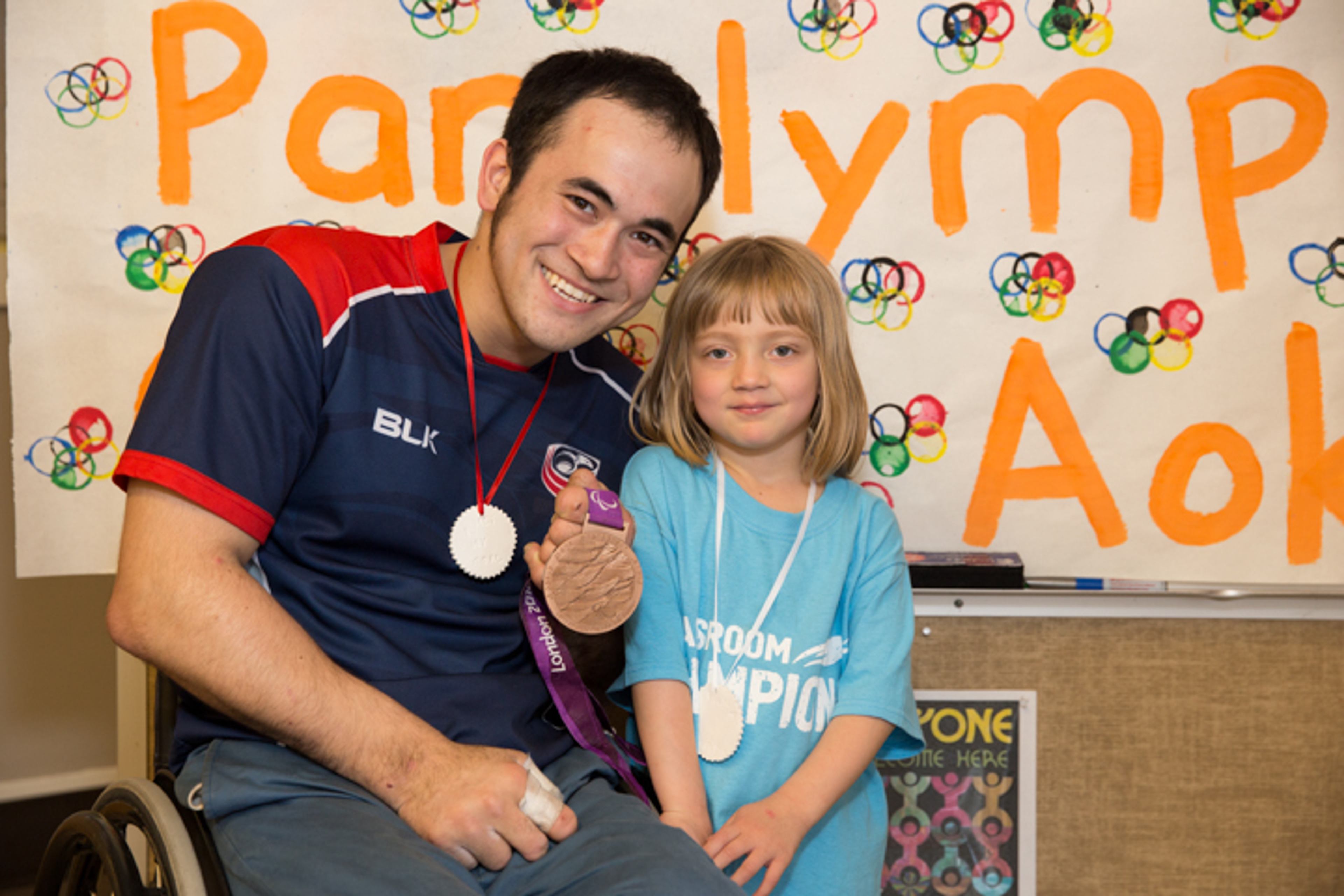 A Paralympic athlete shares his medal with a Classroom Champions student in a classroom celebrating the Paralympics.