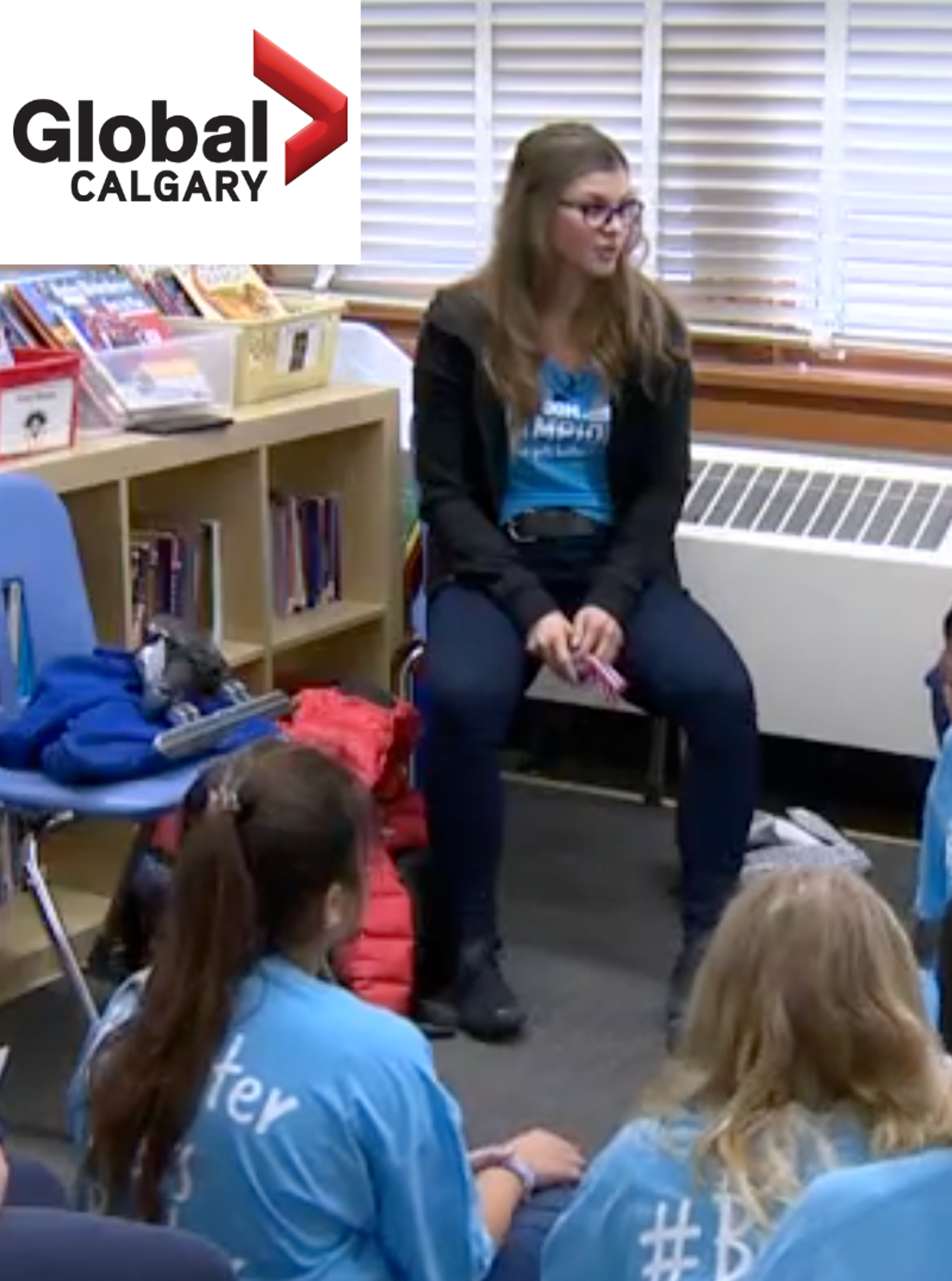 A Classroom Champions mentor speaks with students seated on the floor, as featured on Global Calgary news.