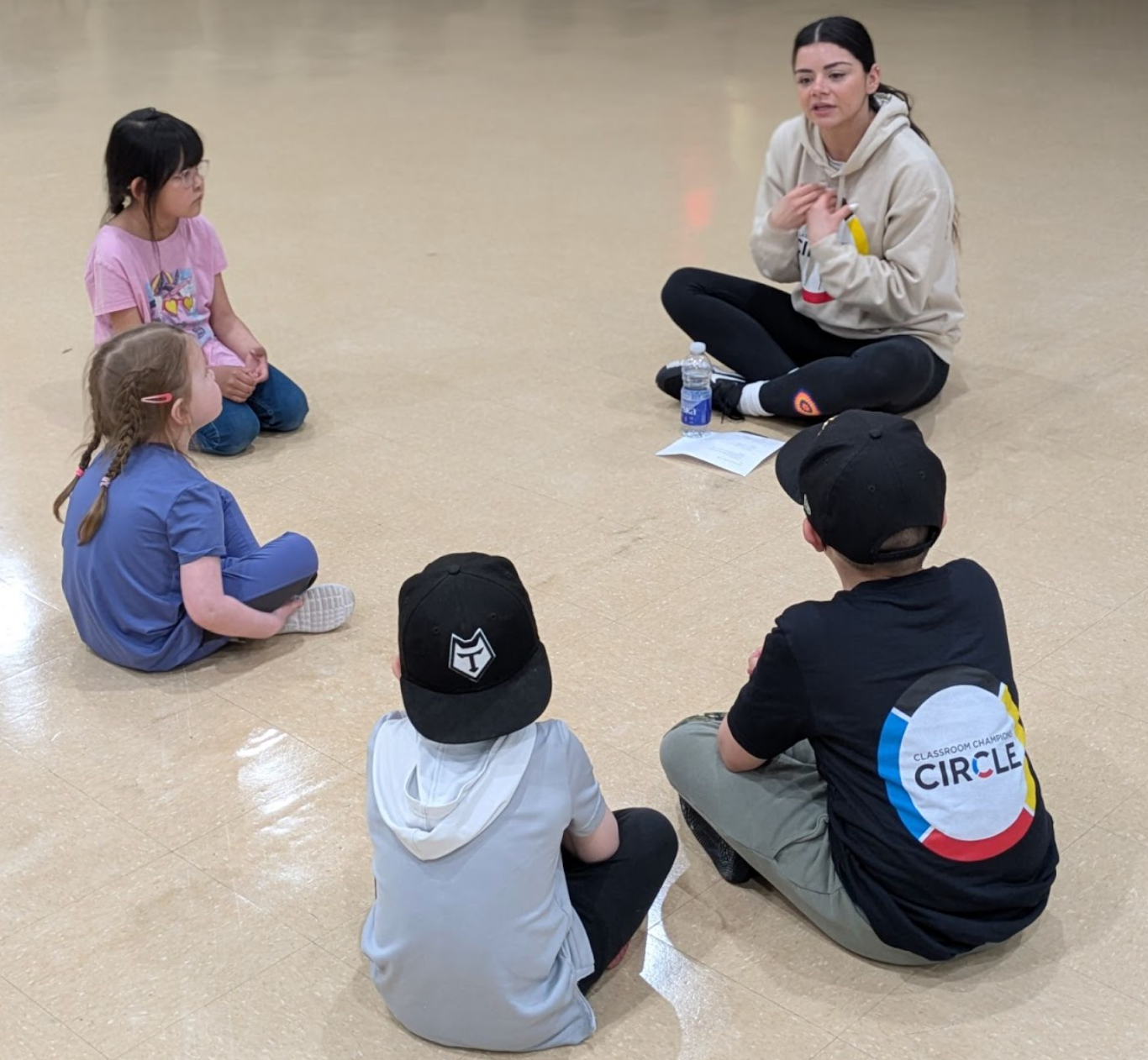 A mentor leads a Classroom Champions Circle discussion with students seated in a circle on the floor.