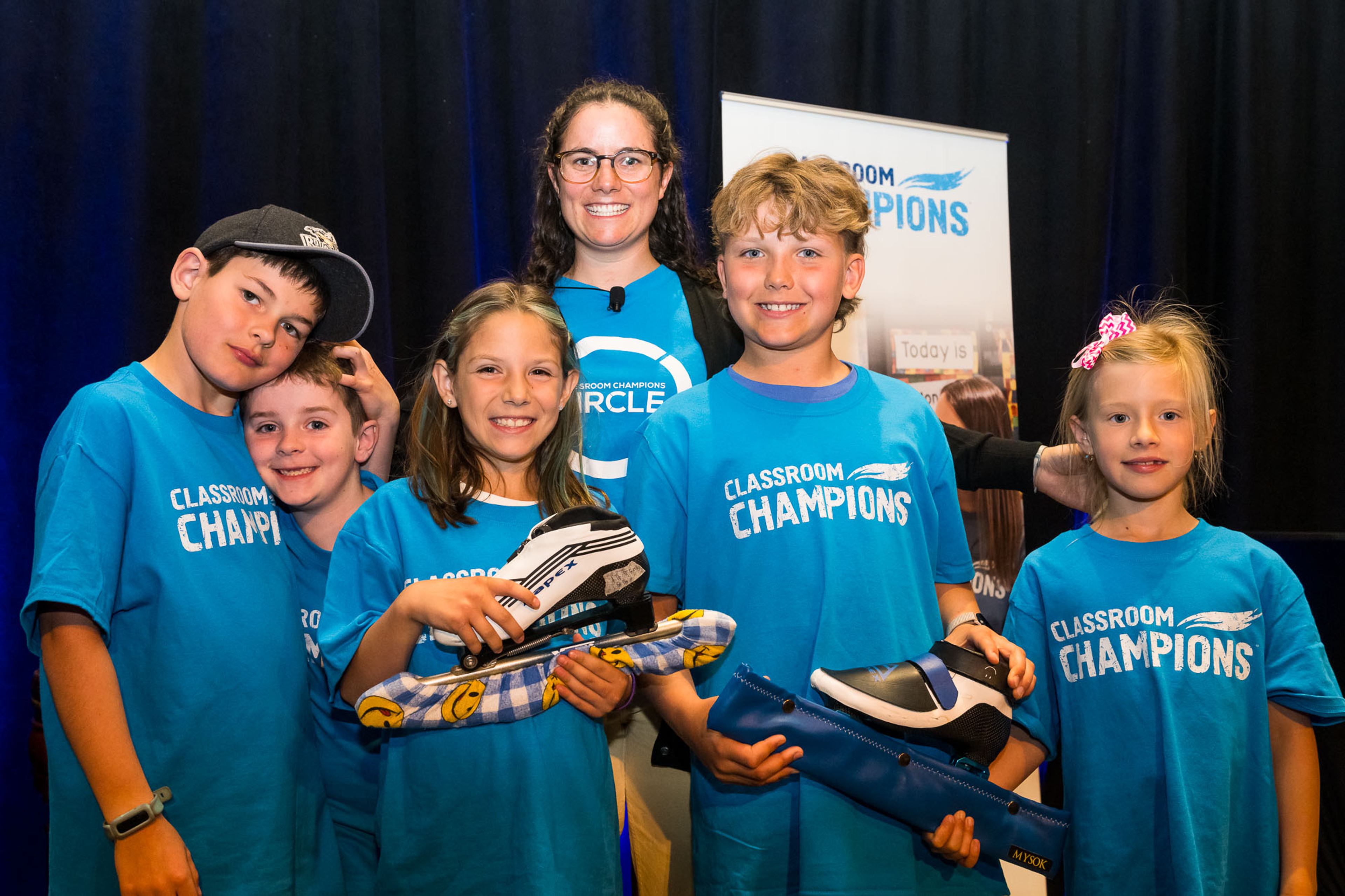 Students in Classroom Champions shirts pose with a mentor, two holding speed skates.