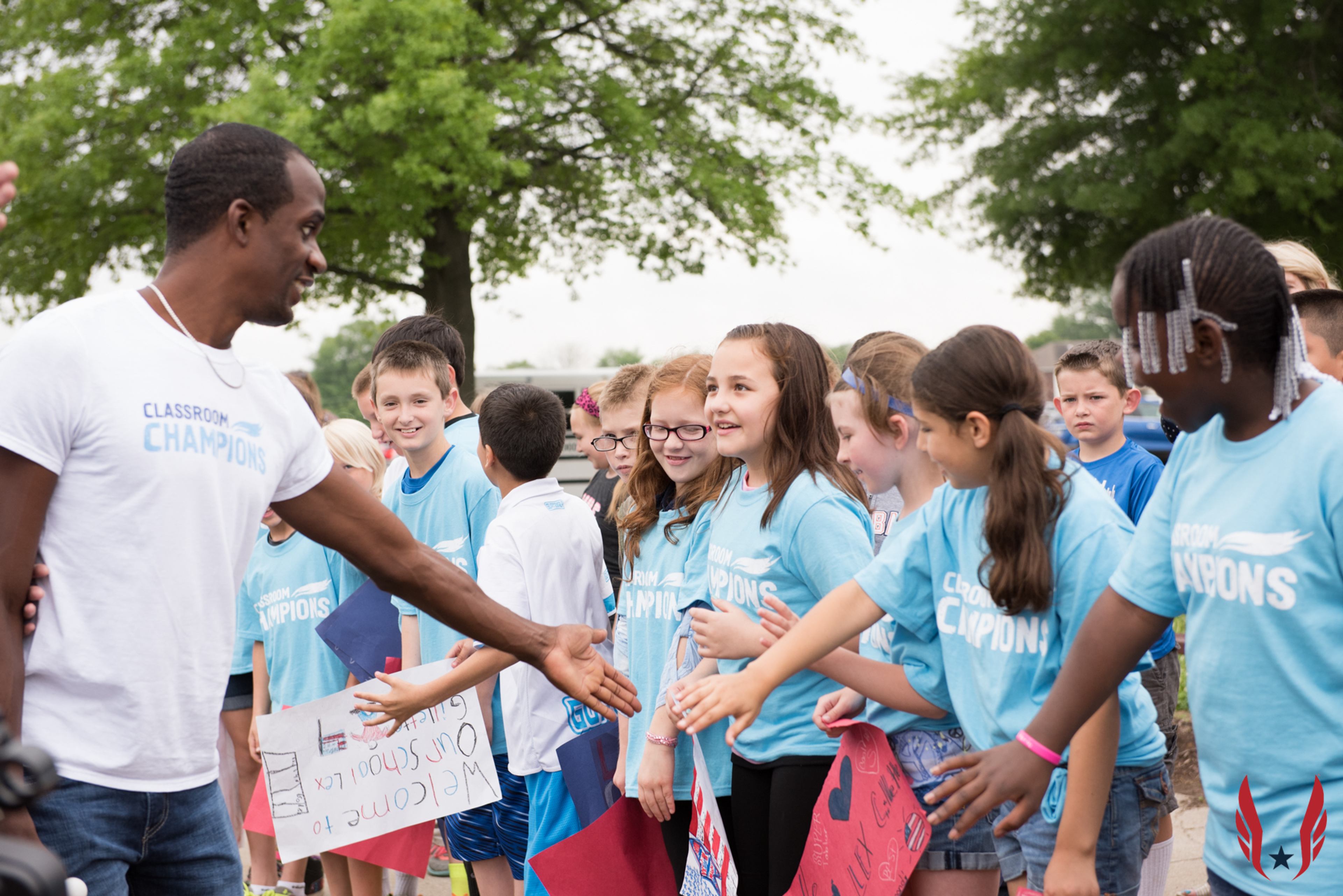 An athlete mentor high-fives students in Classroom Champions T-shirts welcoming him to their school.