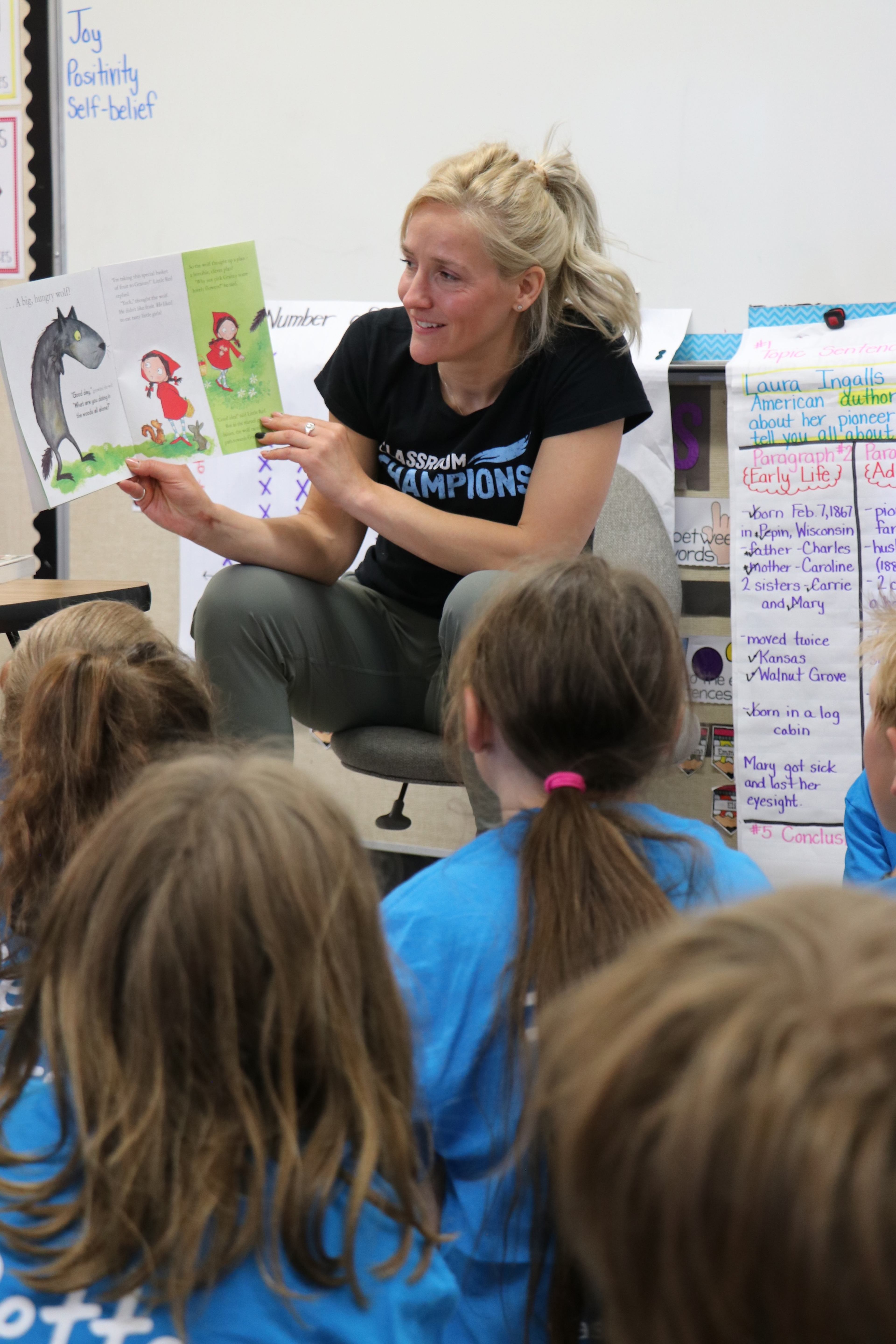 A Classroom Champions mentor reads a storybook aloud to students seated on the classroom floor.