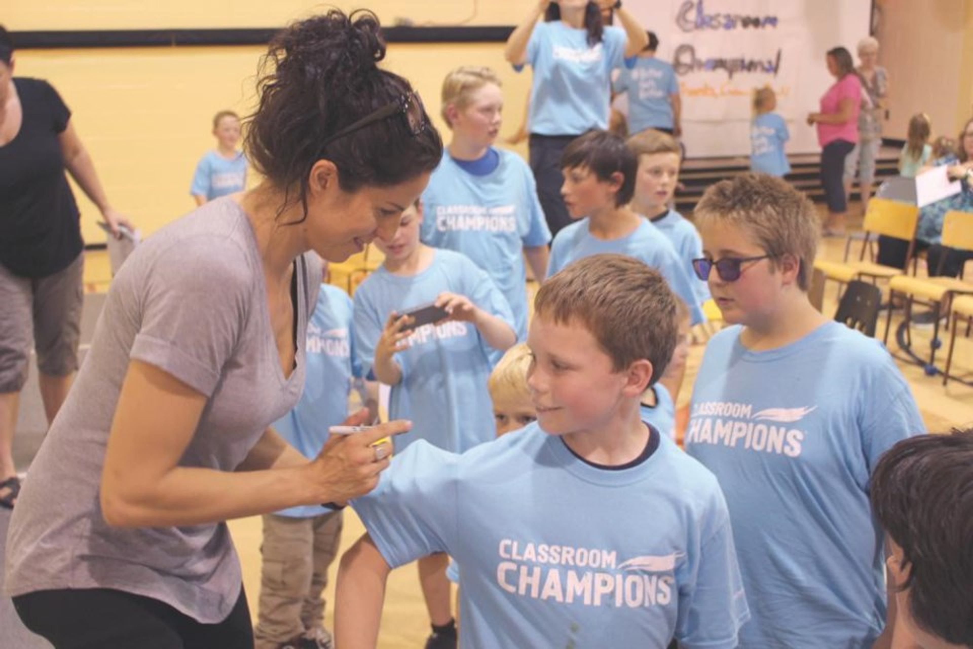 An athlete mentor greets students wearing Classroom Champions T-shirts at a school event.