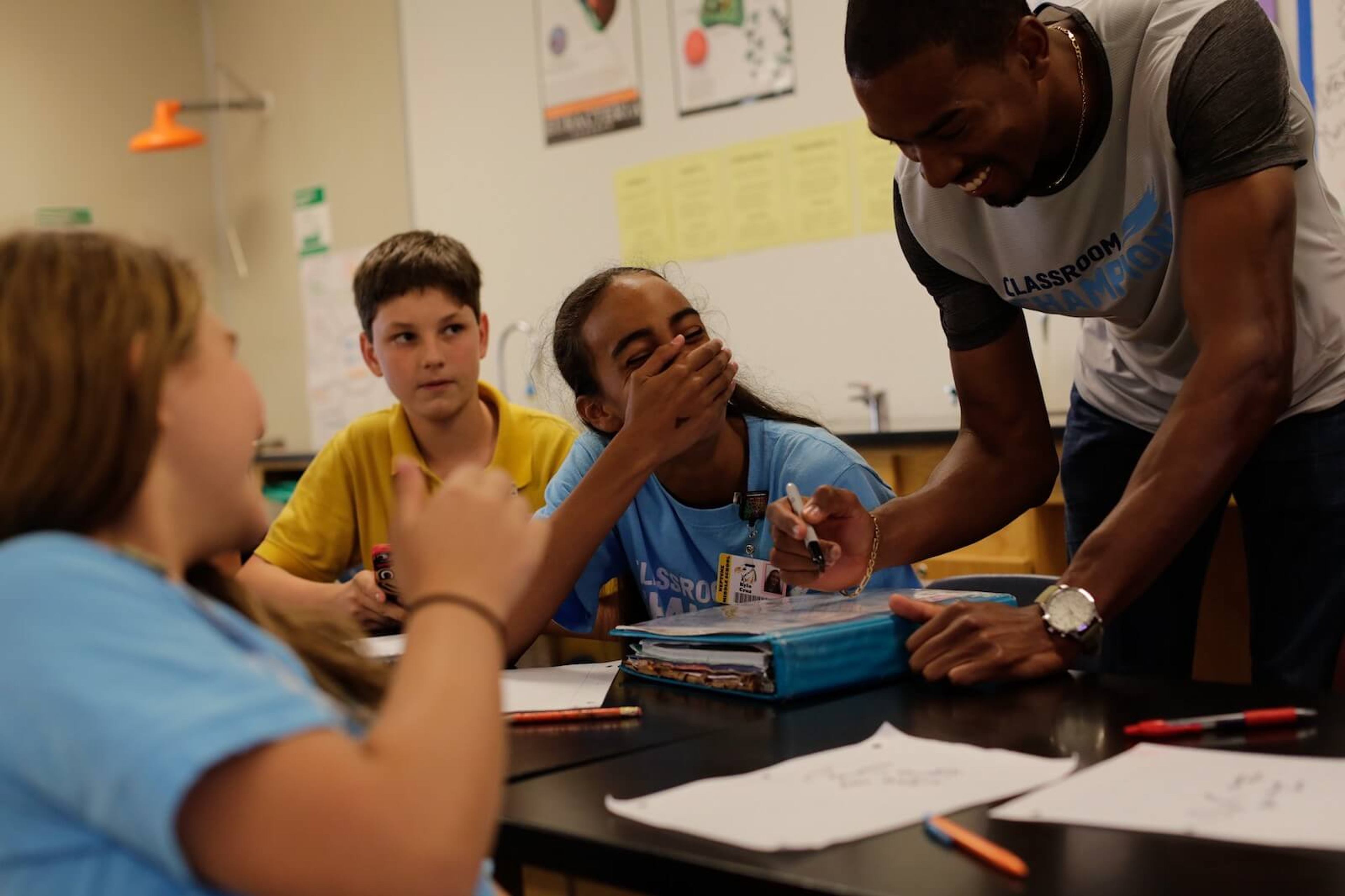 An athlete teaches two laughing girls and a skeptical boy in a yellow shirt