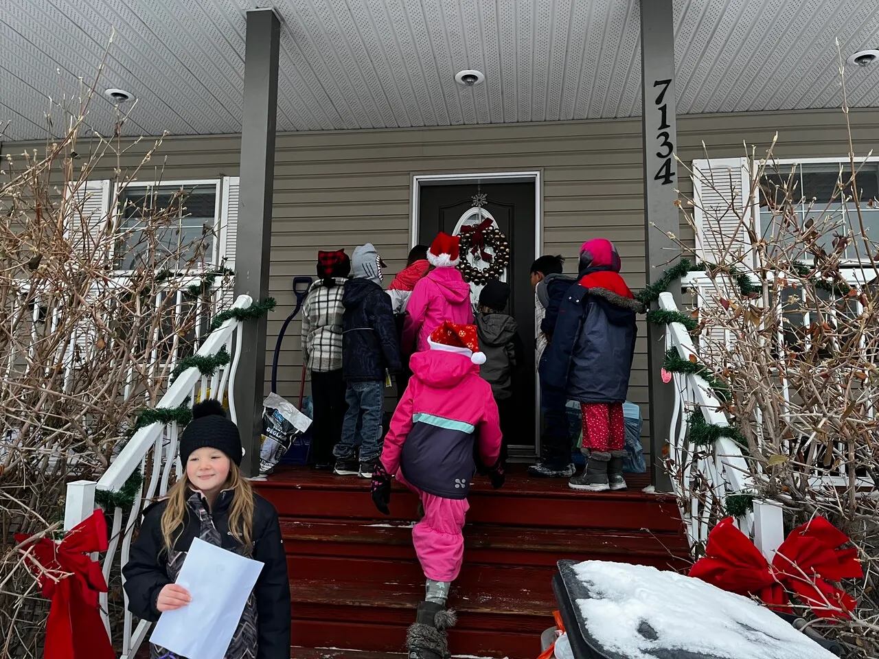 Bundled-up children gather on a snowy porch during a winter service project to deliver something to a home.