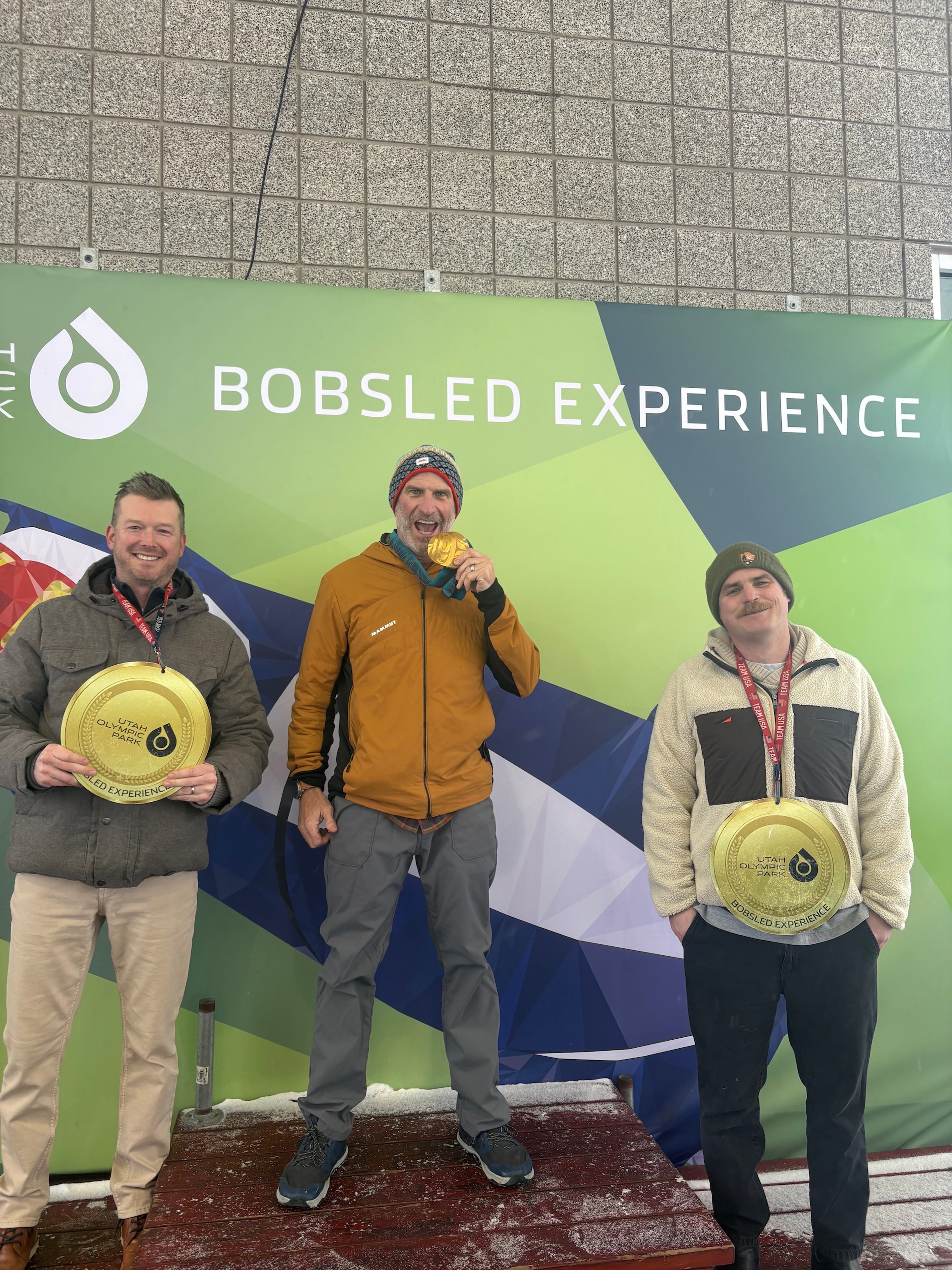Three men celebrate on a podium with medals at the Utah Olympic Park Bobsled Experience.