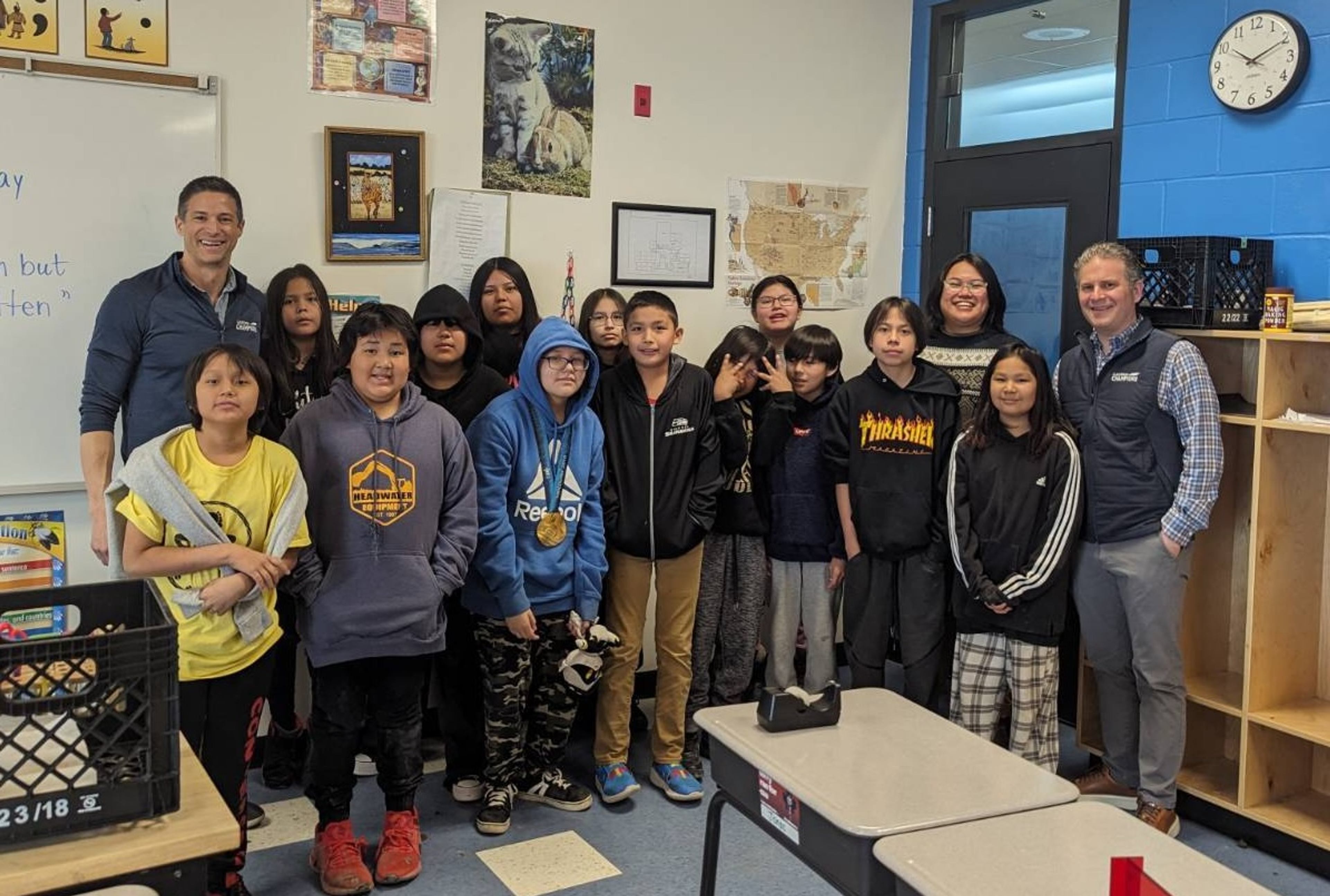 Classroom Champions mentors pose with a group of students in their classroom, one wearing a medal.