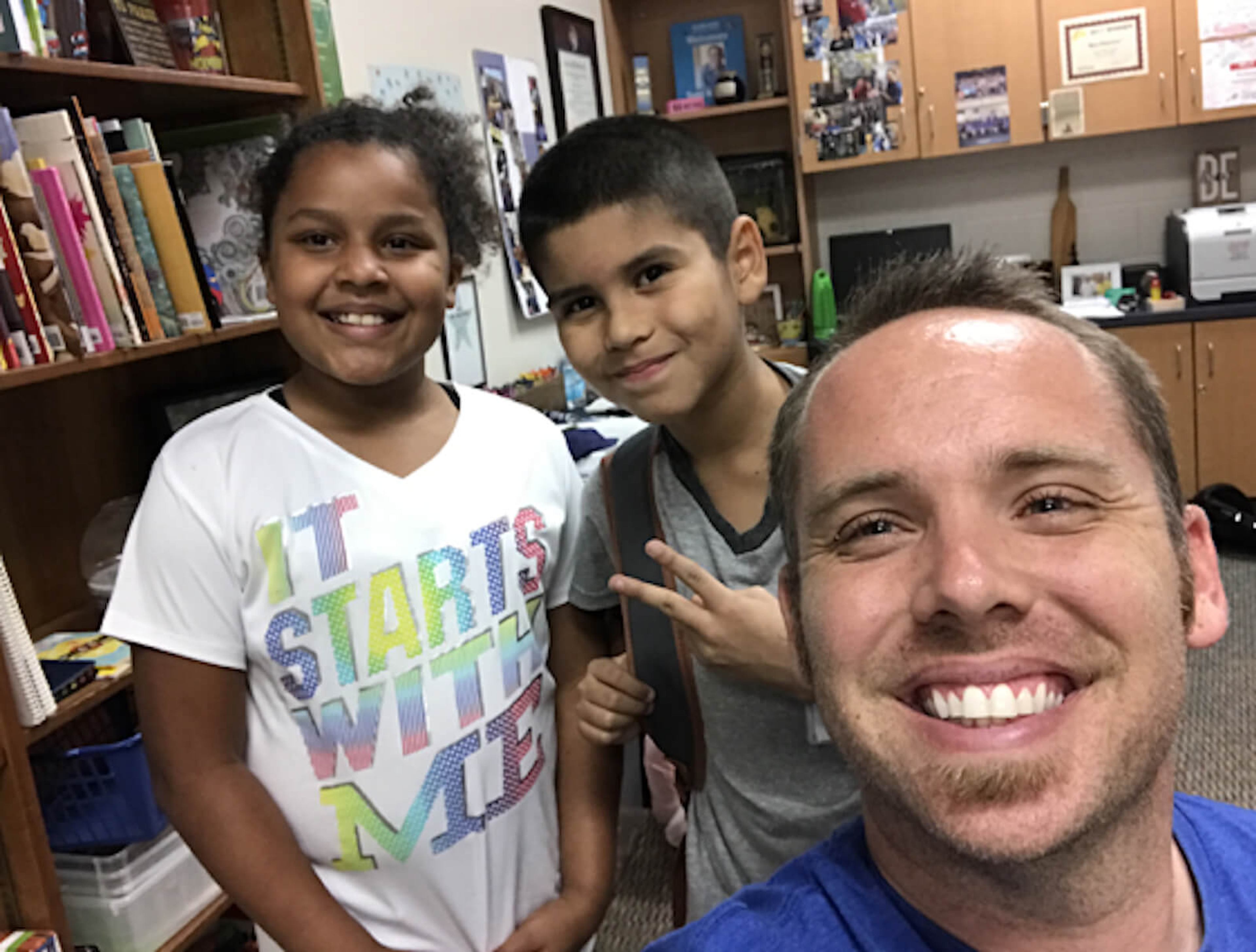 Two kids and a man smile in a classroom