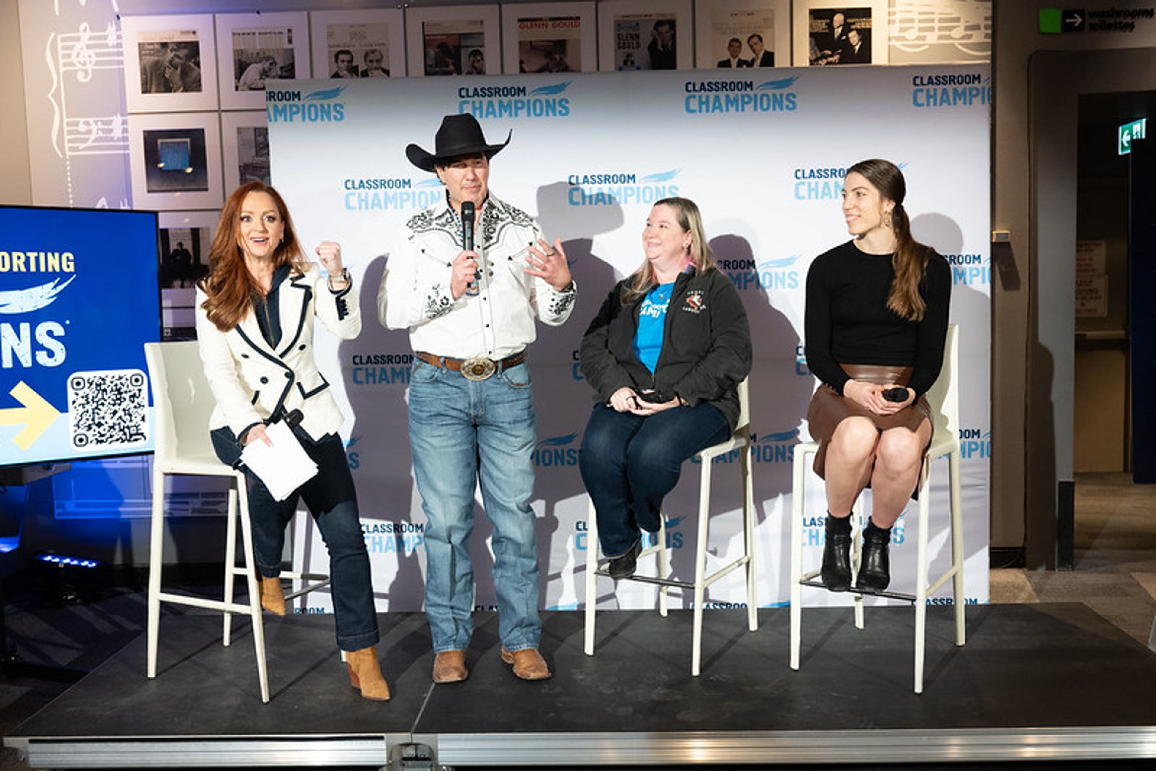 Panelists speak on stage at a Classroom Champions event with a branded backdrop.