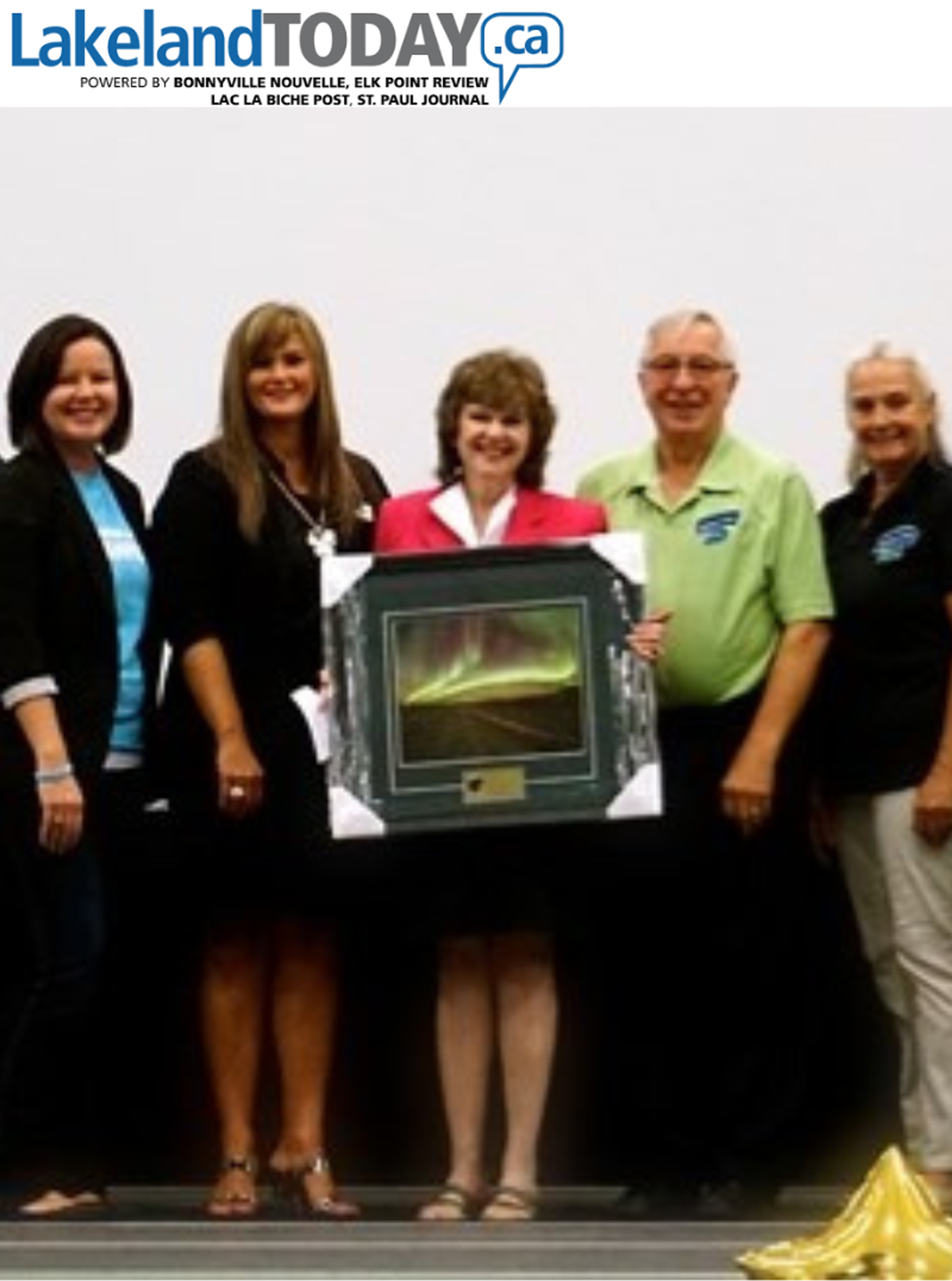 Group presenting a framed northern lights artwork as an award at a Lakeland Today event.