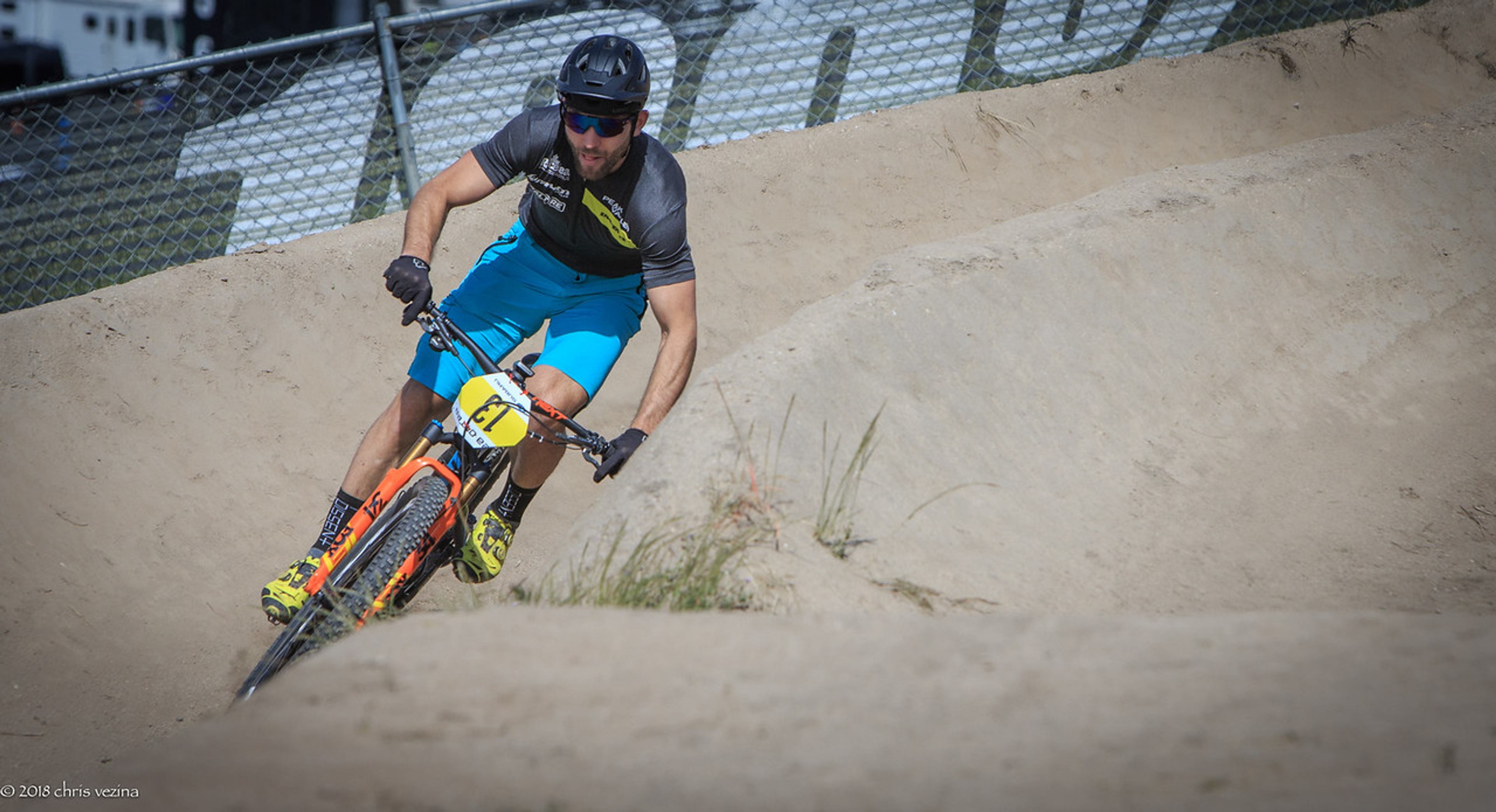 Mountain biker leans into a banked dirt turn during a race.