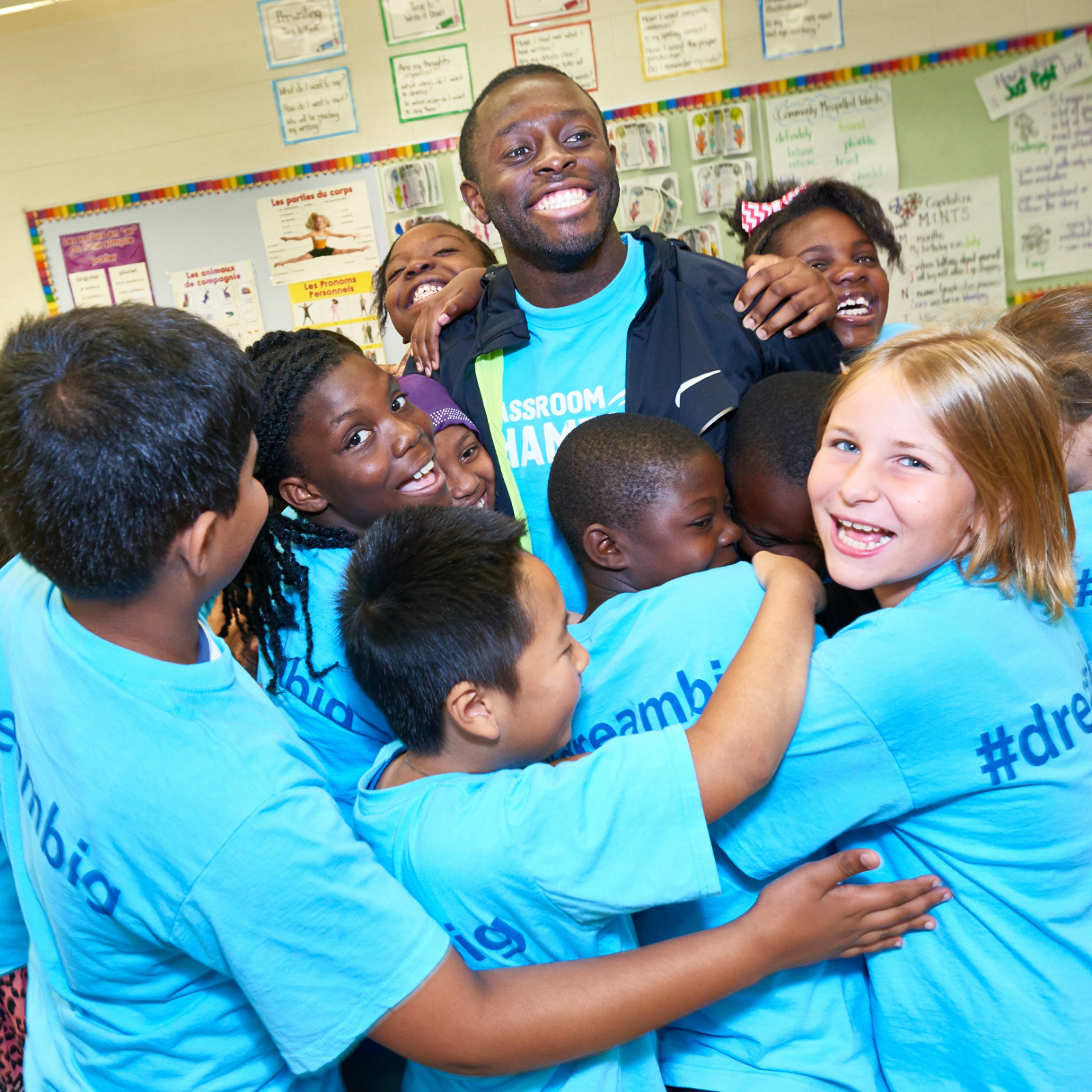 A Classroom Champions mentor is surrounded in a joyful group hug by students wearing #DreamBig shirts.