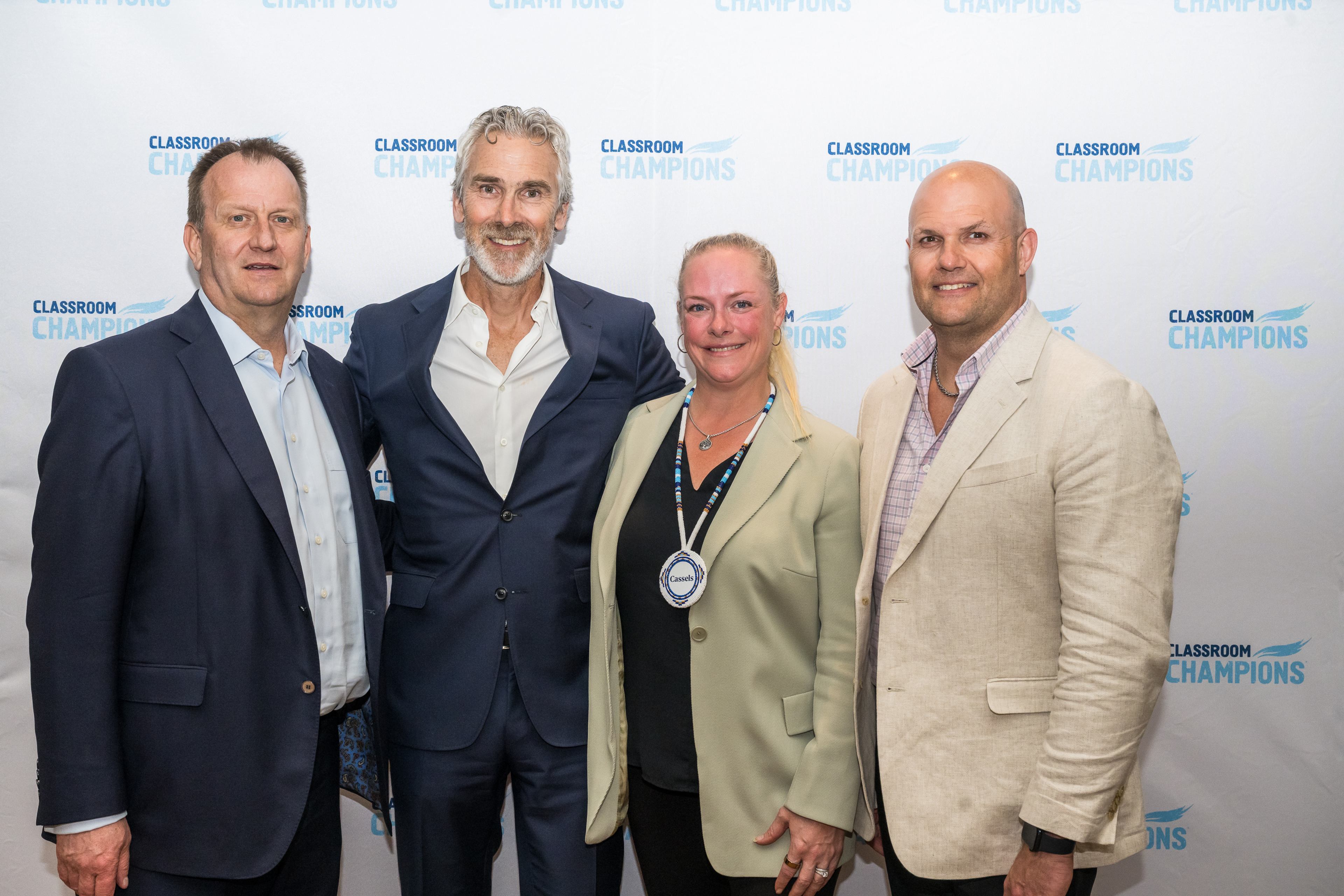 Four supporters pose together at a Classroom Champions event in front of a branded step-and-repeat backdrop.