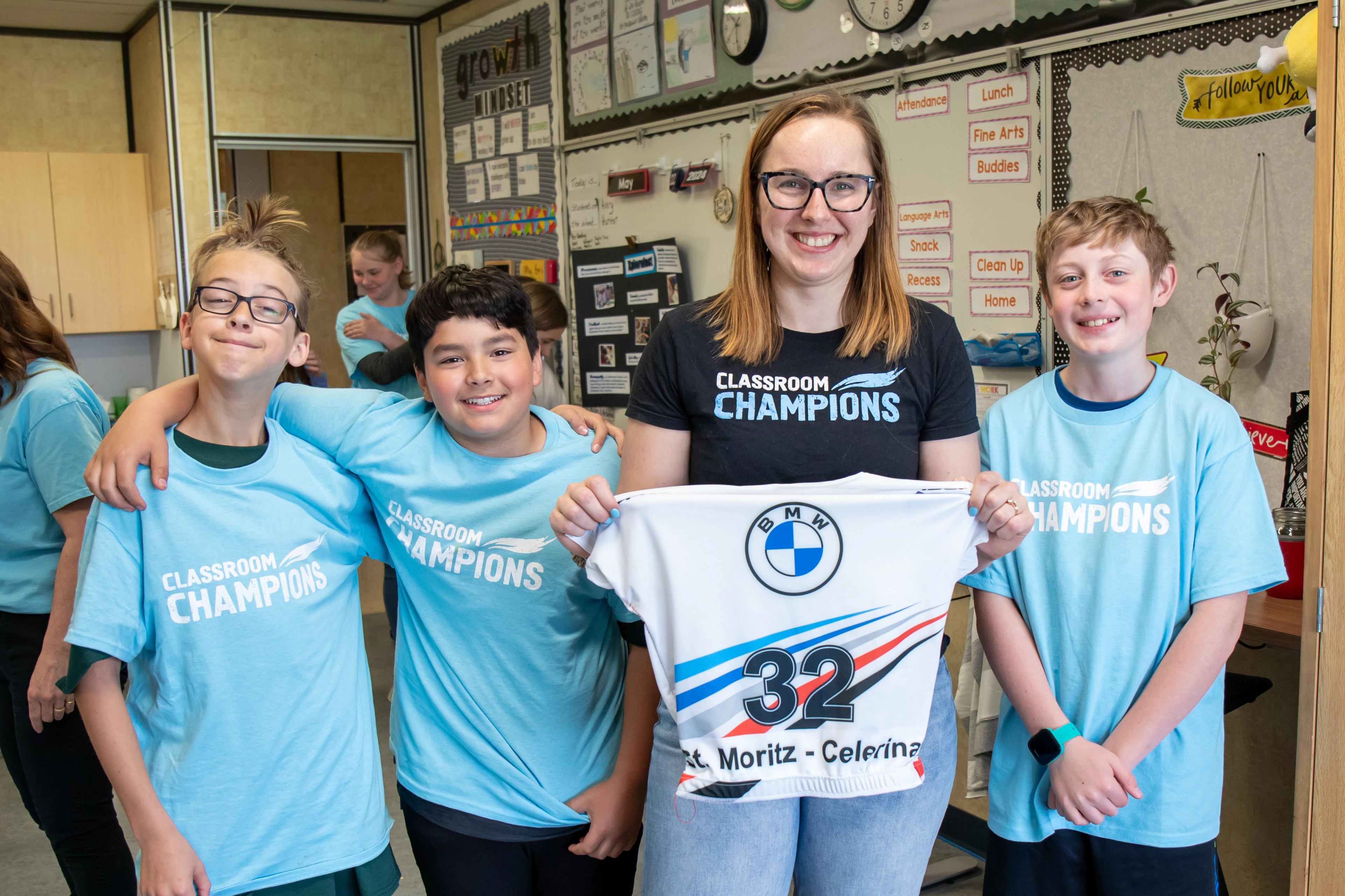 A teacher and students in Classroom Champions shirts hold a BMW race bib during Grace Dafoe's mentor visit.